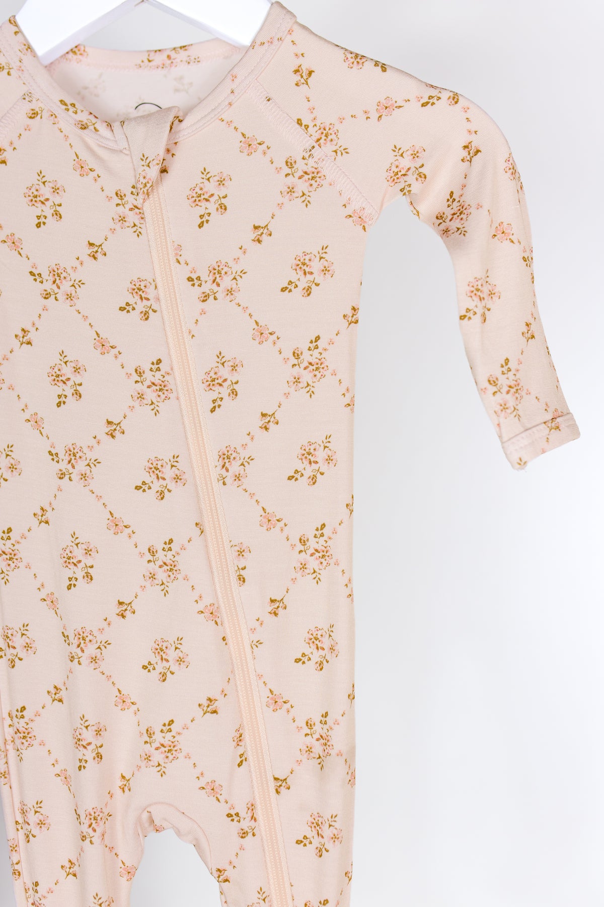 A keepsake / one piece zipper long-sleeve bamboo baby sleeper in light pink with a subtle floral pattern hangs on a white hanger against a plain white background.