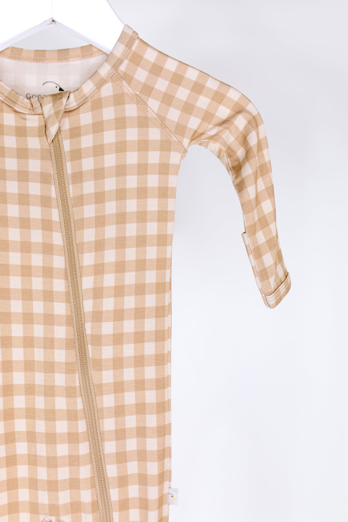 A “teddy bear check / one piece zipper” newborn onesie in beige and white checkered pattern, featuring a convenient zipper closure, hangs on a white hanger against a plain white background. Only one sleeve and part of the body are visible.