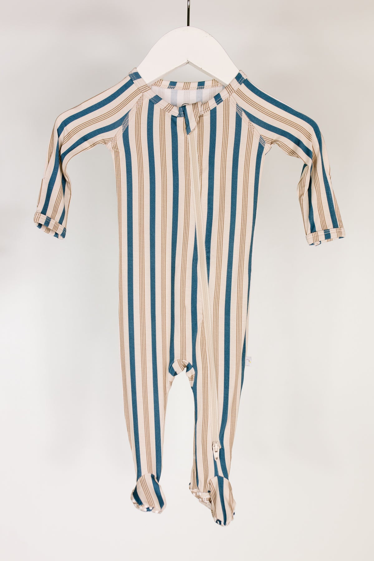 A shoreline / one piece zipper featuring long sleeves and blue and beige vertical stripes hangs on a white hanger against a plain white background.