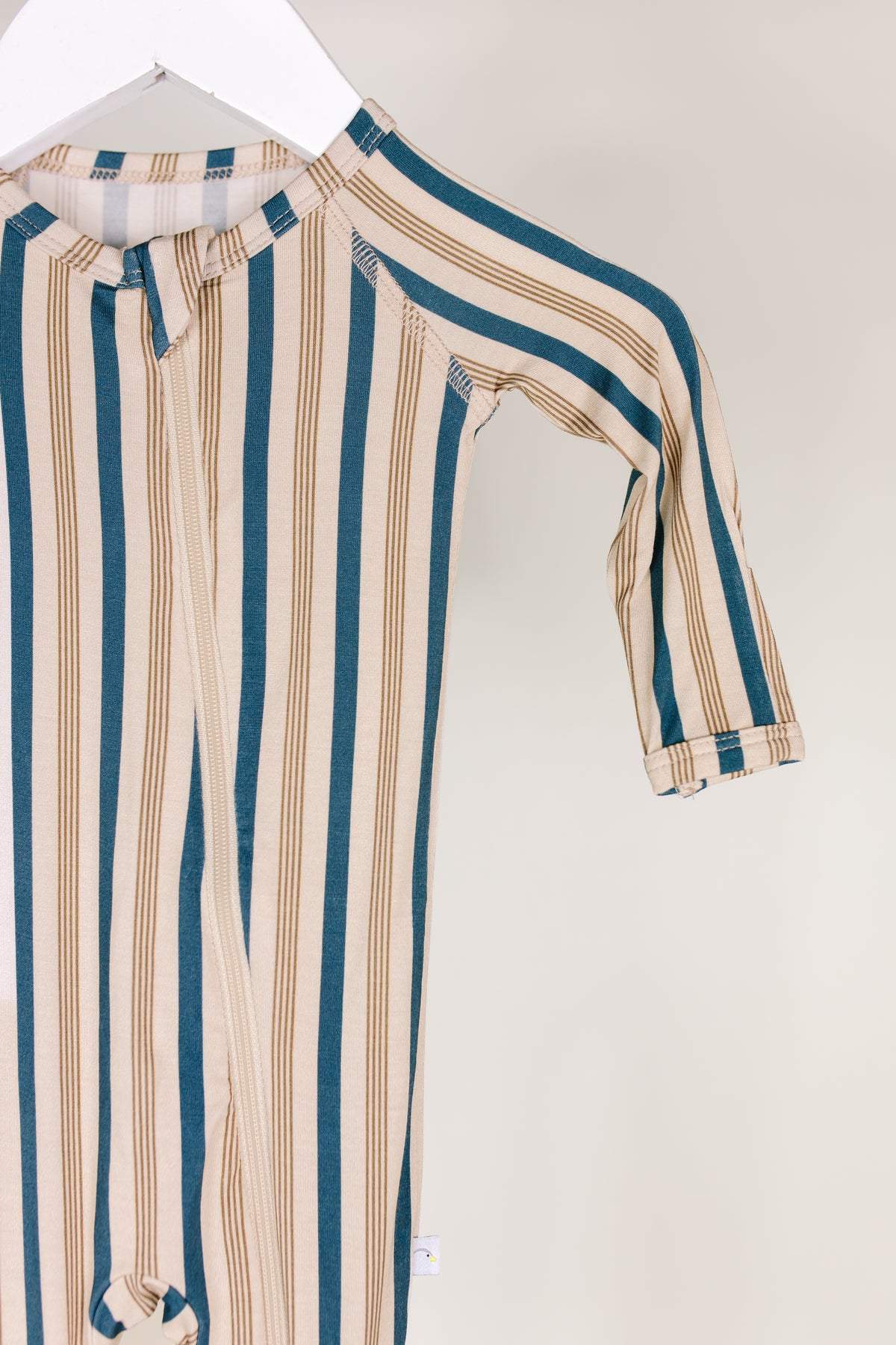 The shoreline / one piece zipper, a long-sleeve bamboo baby romper featuring vertical teal and beige stripes, hangs on a white hanger against a plain light background, providing the cozy softness of bamboo baby pajamas for your little one.