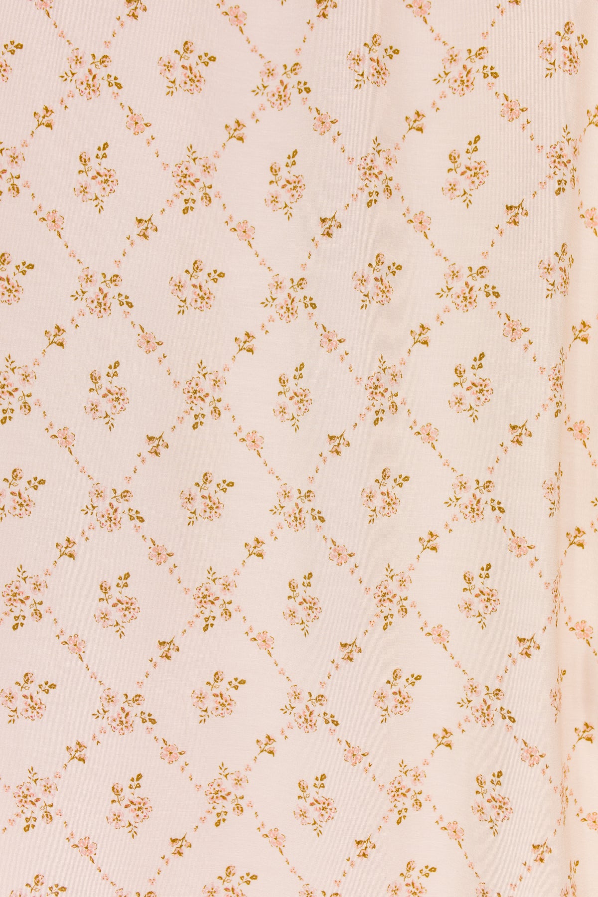 The keepsake / swaddle features a light pink bamboo fabric adorned with a diamond lattice pattern, highlighted by small clusters of yellow and pink flowers at each intersection. The delicate floral print is evenly spaced across the swaddle, offering a soft and charming appearance.