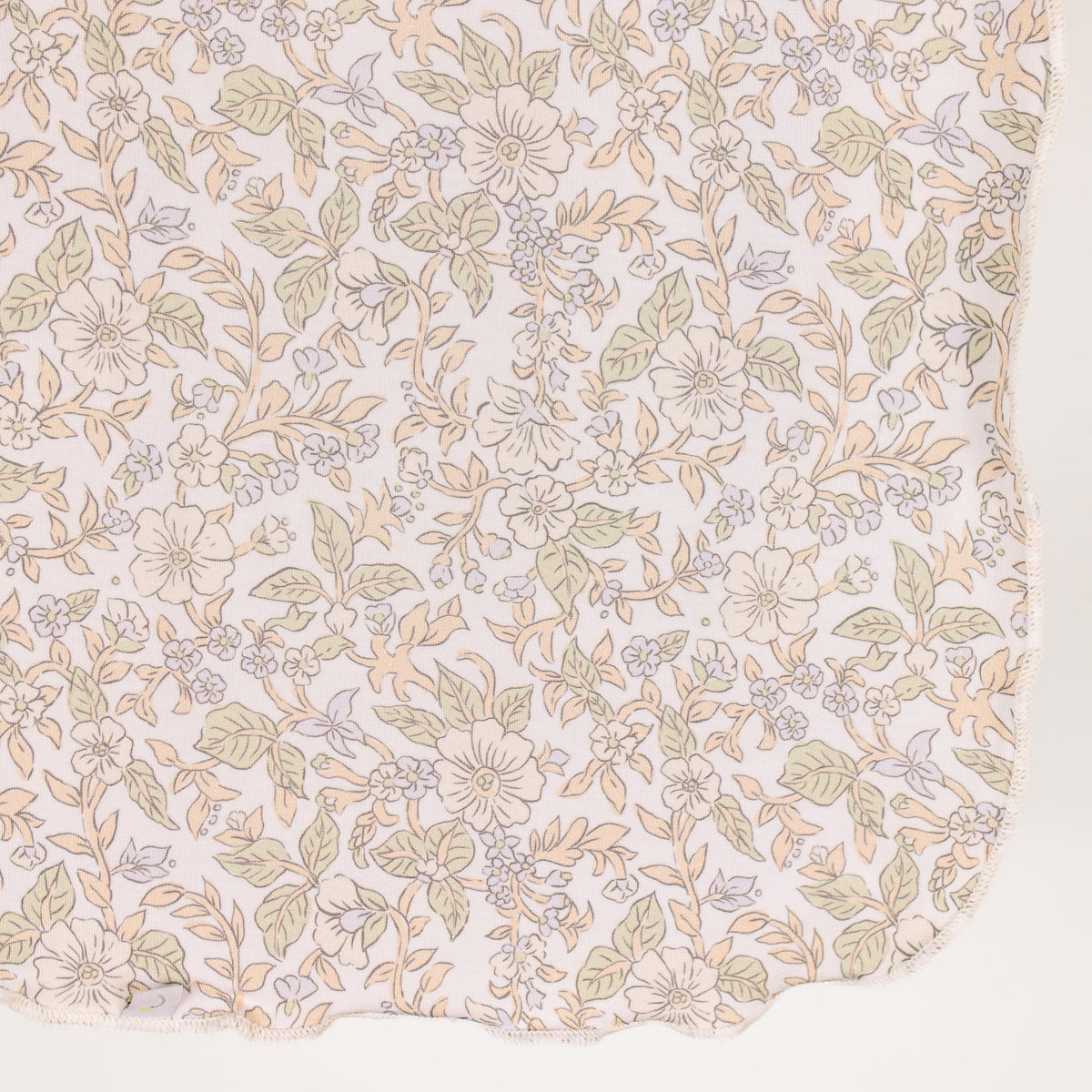 A close-up of the heirloom / swaddle showcases its delicate floral print, featuring pastel flowers and green leaves on a light background, with scalloped edges visible at the bottom. This single-layered bamboo swaddle highlights the intricate details of its charming design.