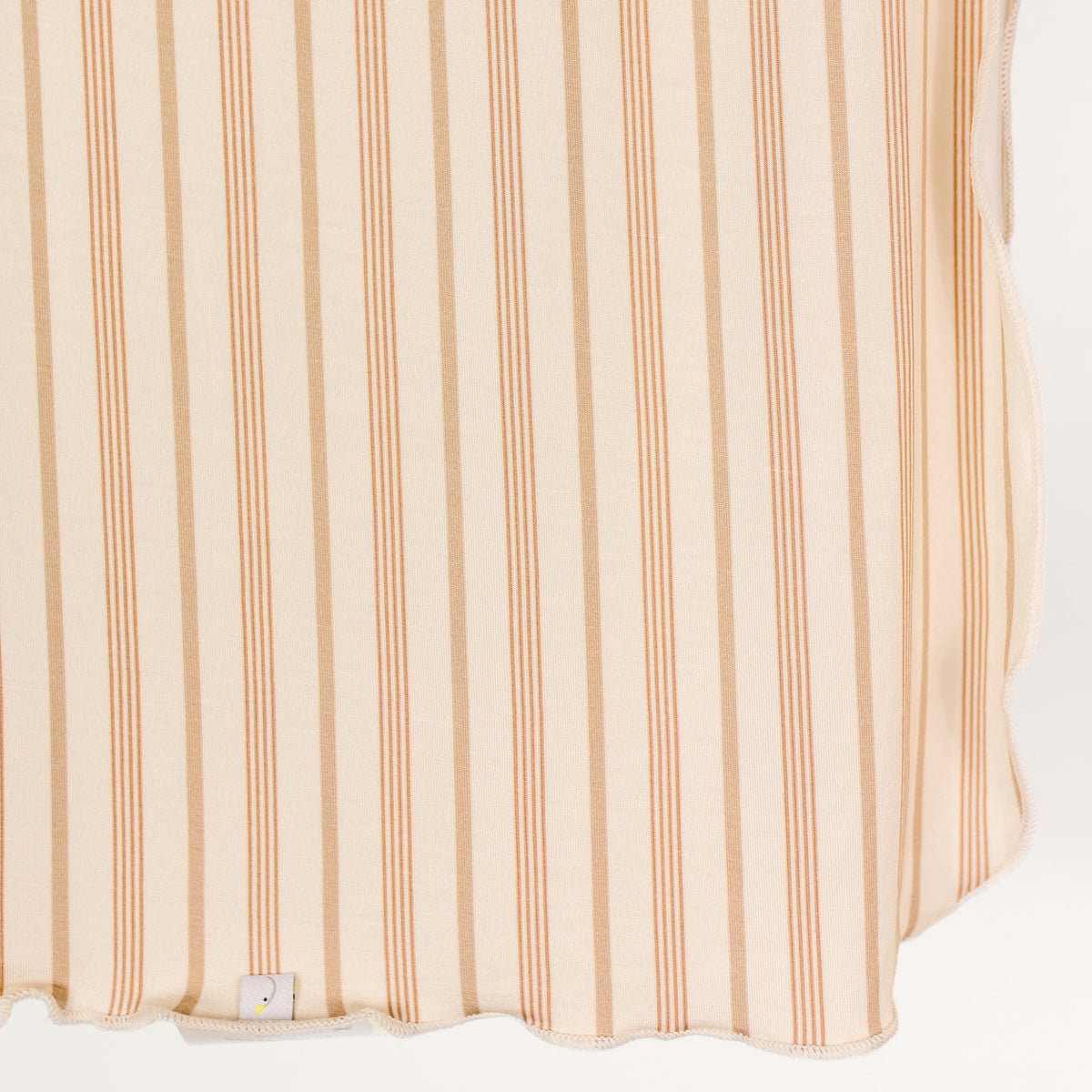 Beige fabric with vertical peach-colored stripes reminiscent of a tan and cream stripe; this single layered toast and honey / swaddle features a small white tag visible at the bottom edge.