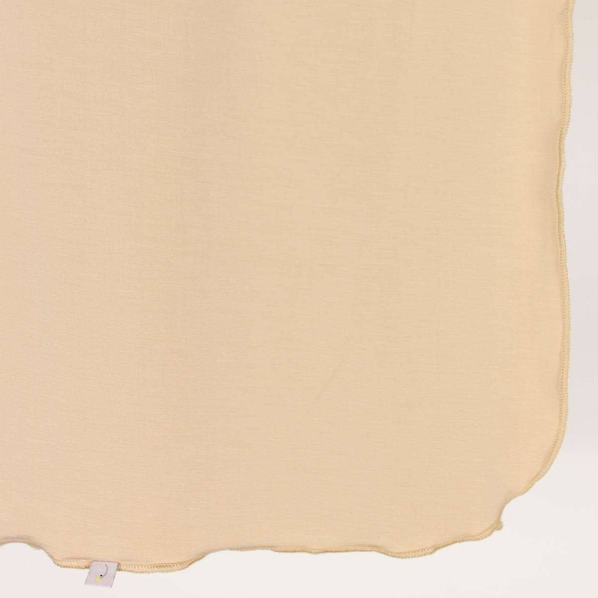 A close-up of the vanilla cream / swaddle, featuring a beige, semi-transparent viscose fabric with gently wavy edges, draped vertically. A small white tag appears at the bottom left corner.