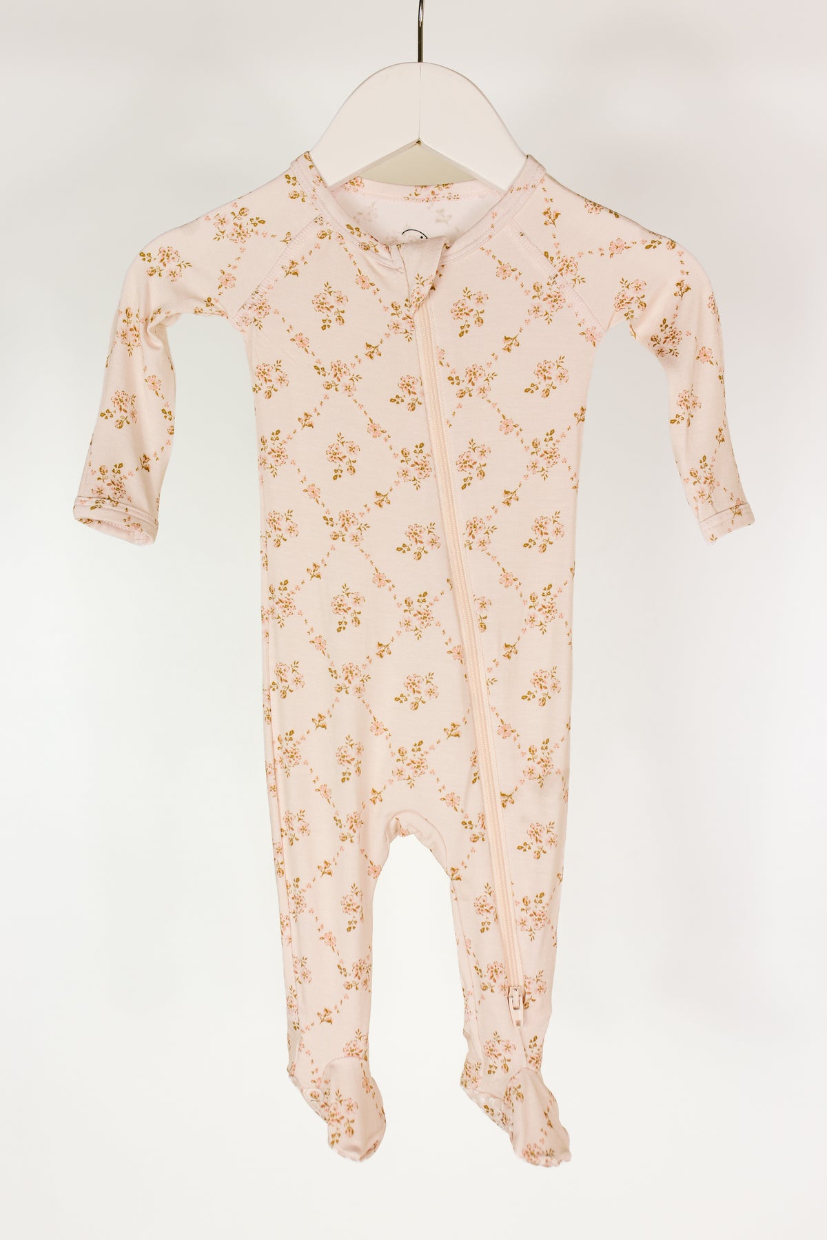 A light pink keepsake / one piece zipper bamboo baby pajamas onesie featuring a subtle floral pattern and a diagonal zipper, displayed on a white hanger against a plain white background.