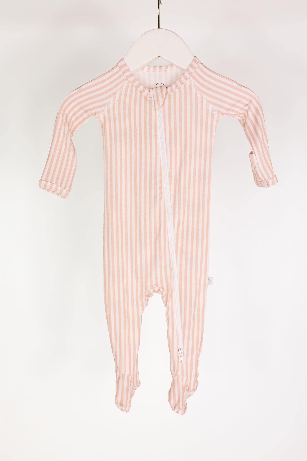 A heritage / one piece zipper pink and white striped bamboo baby pajamas onesie with long sleeves and covered feet, hanging on a white hanger against a plain white background.
