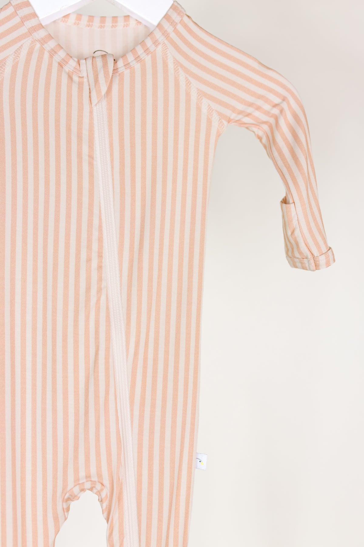 A heritage / one piece zipper bamboo baby pajamas onesie in pink and white stripes, featuring long sleeves and a front zipper, is displayed on a white hanger against a light background.