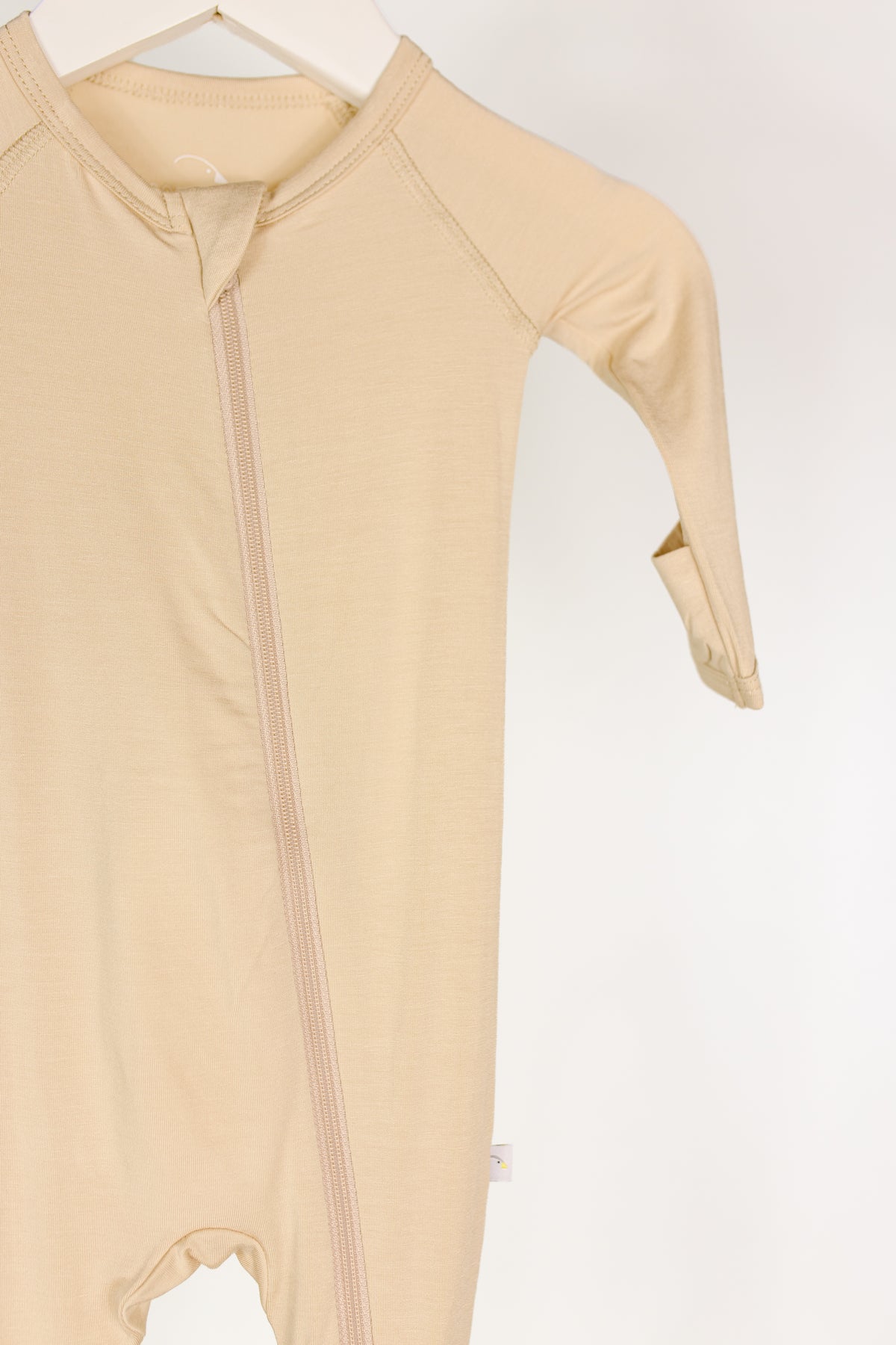 Vanilla cream one piece zipper for newborns with long sleeves, shown on a hanger against a white background. Only part of the bamboo baby pajamas is visible, featuring an angled zipper and one folded-up sleeve.