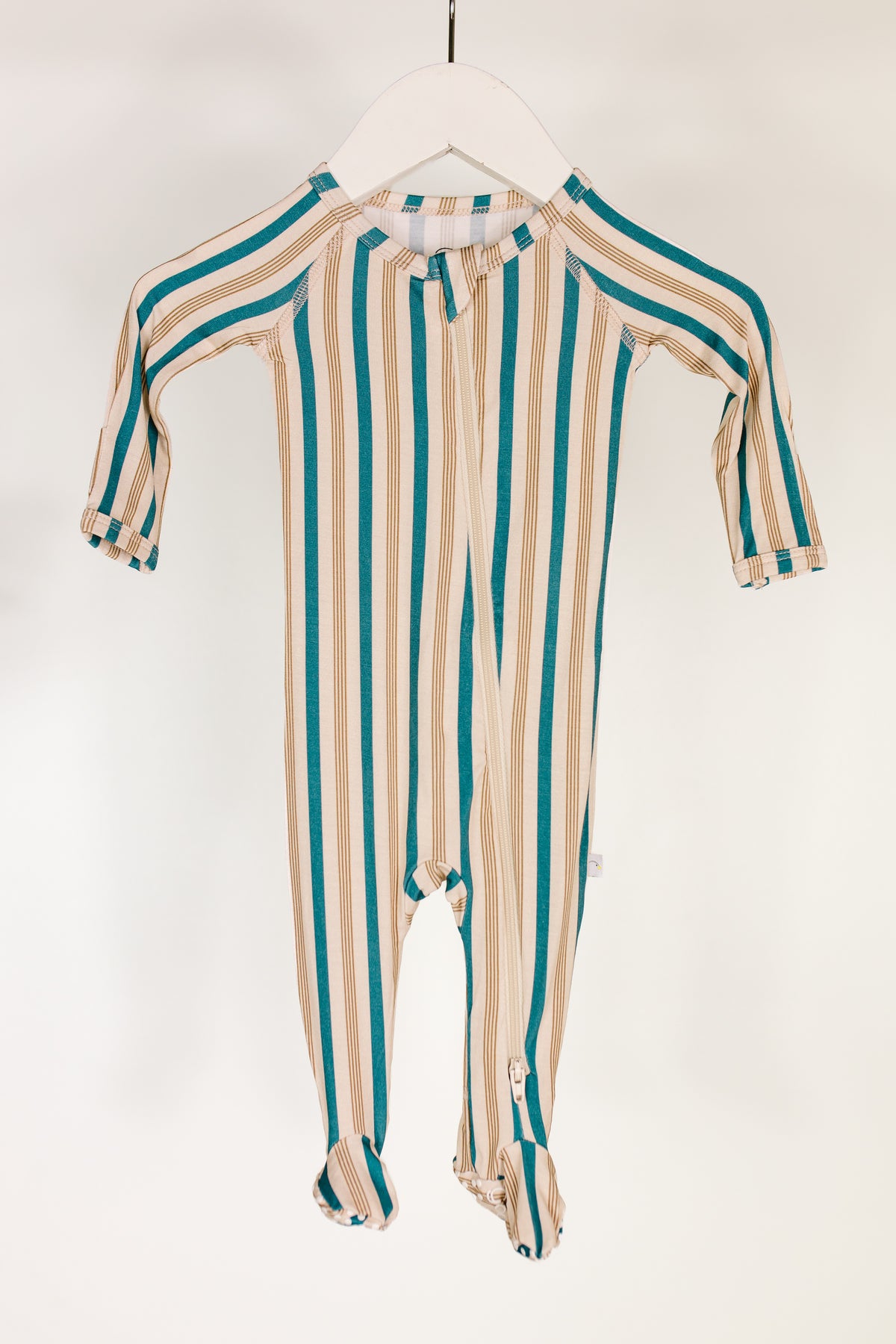 A shoreline one piece zipper, featuring long sleeves and full foot coverage in vertical blue, tan, and white stripes, hangs on a white hanger against a plain white background.