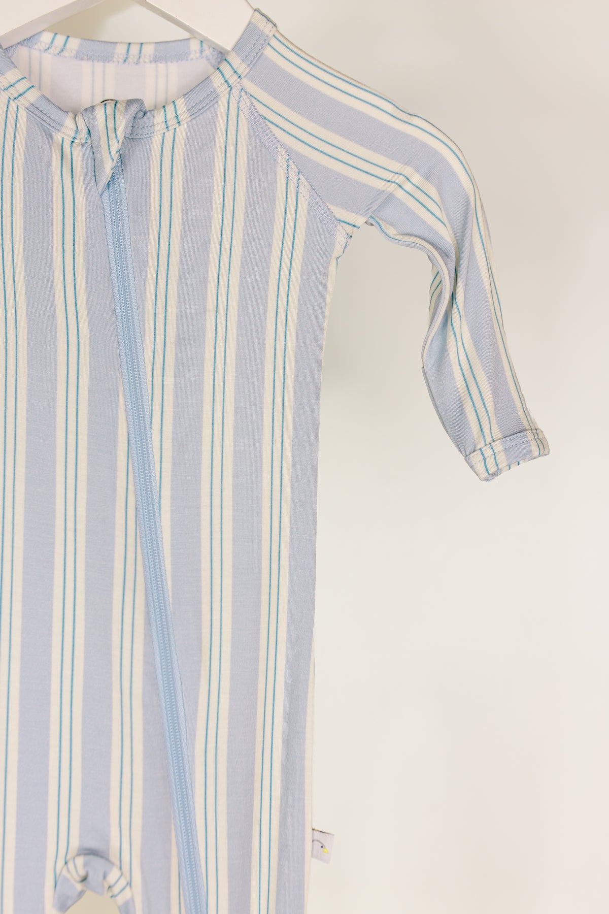 A haven one piece zipper, featuring blue and white stripes, long sleeves, fold-over mittens, and a convenient diagonal zipper, is hanging on a white hanger against a plain background.