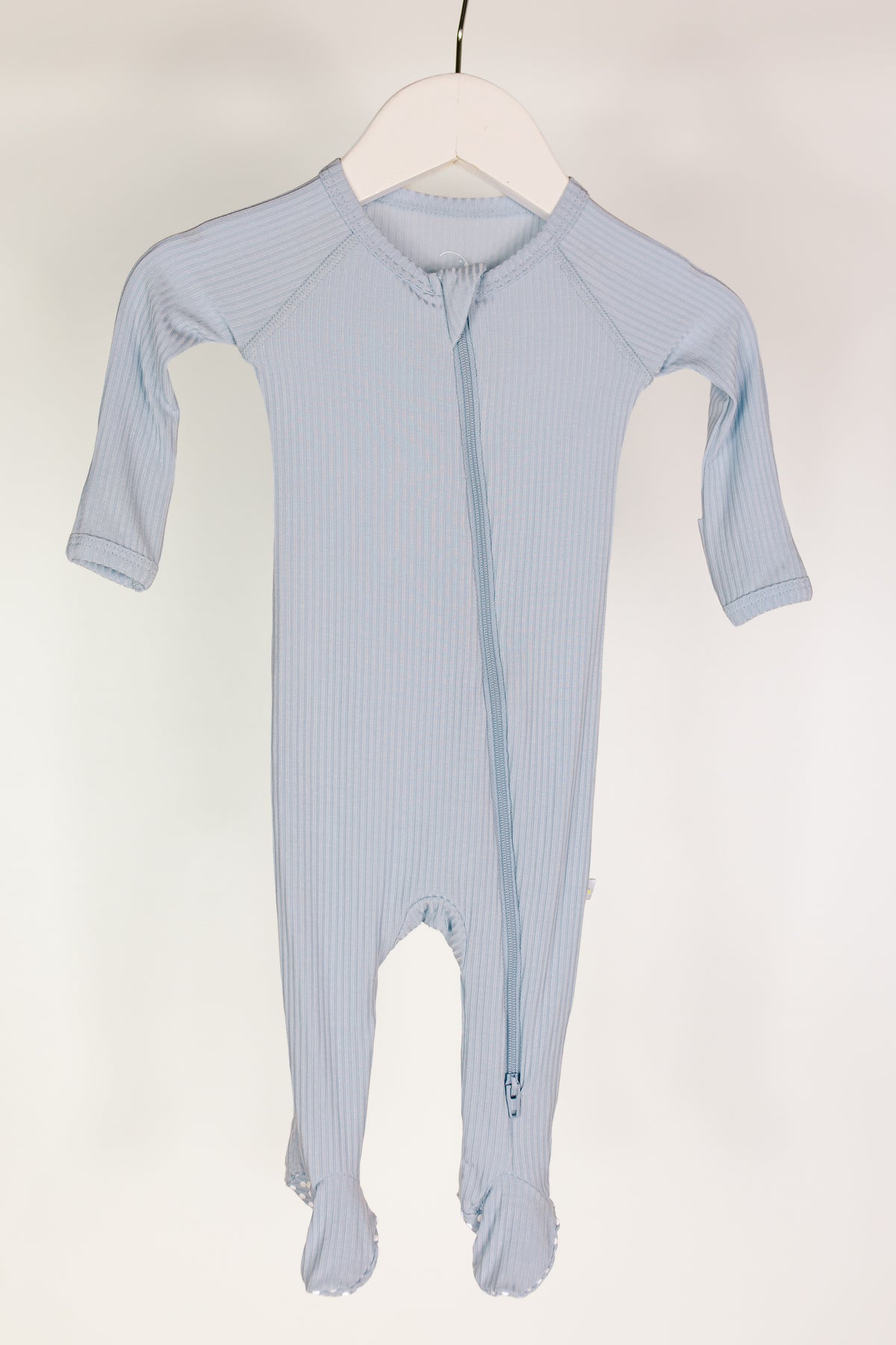 A light blue “cove / one piece zipper” baby sleeper featuring long sleeves, a footed design, and a diagonal zipper, displayed on a white hanger against a plain white background—perfect as cozy newborn footed pajamas.
