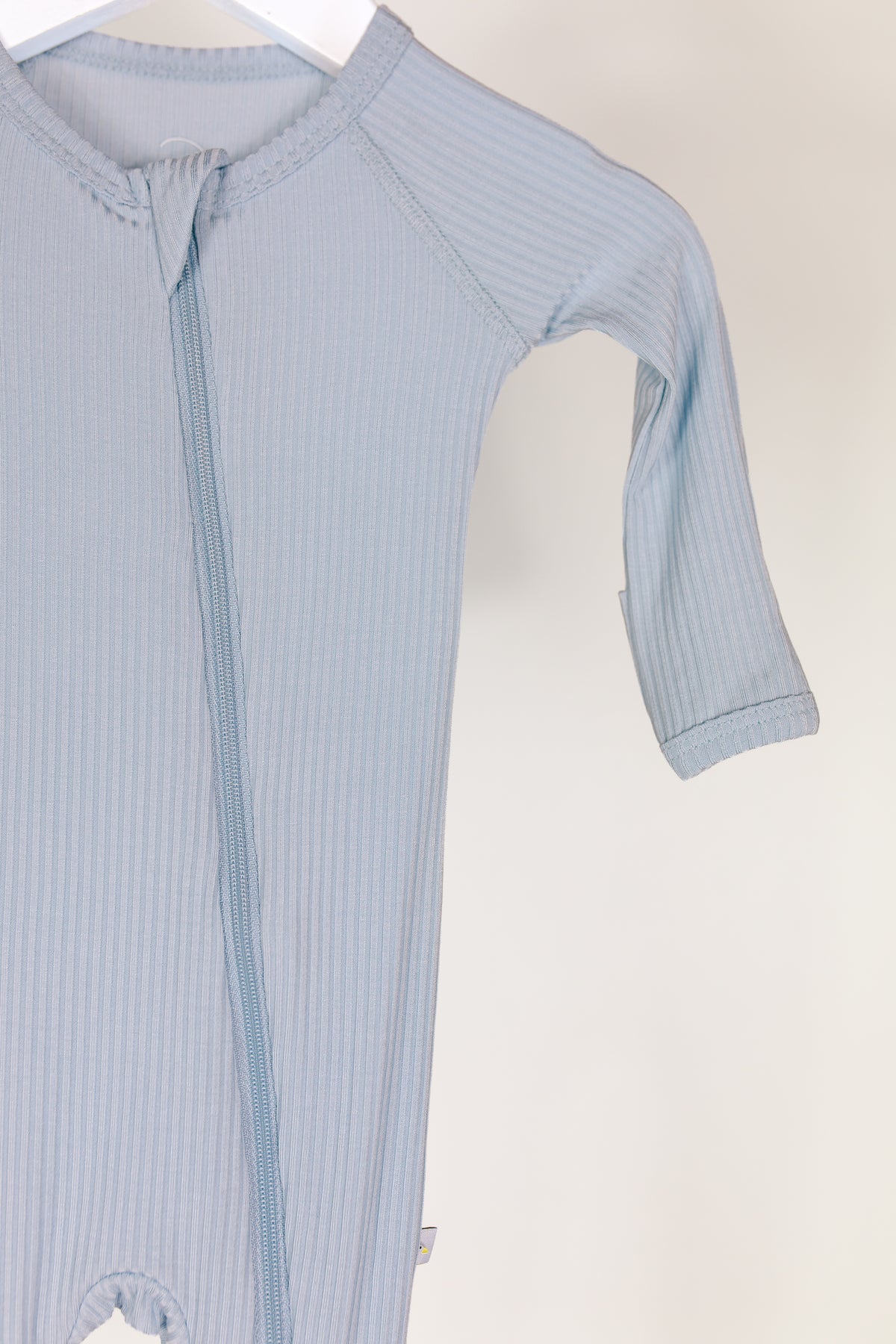 Introducing the cove / one piece zipper: a light blue ribbed bamboo baby sleeper with long sleeves and a front zipper, elegantly draped on a hanger. This cozy zippered one piece is shown partially, displaying just the top half and one sleeve against a simple, light background.