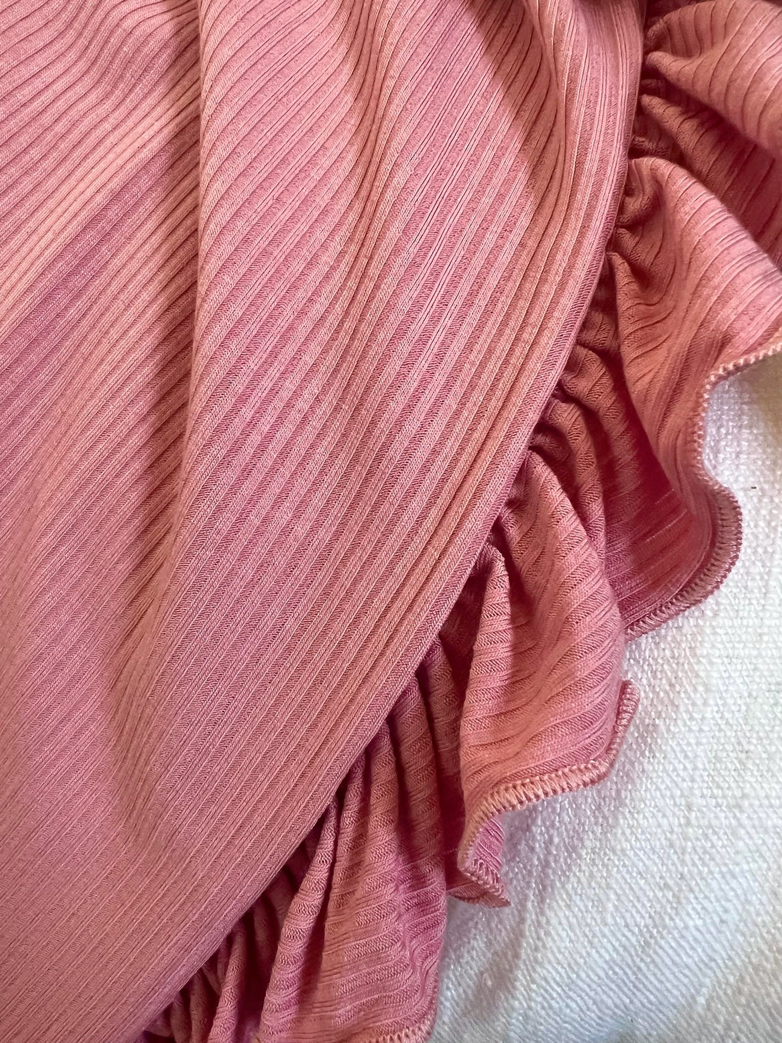 Close-up of the peony / ruffle blanket, featuring ribbed fabric and ruffled edges, draped over a light-textured surface. The luxurious folds and unique texture of this stylish blanket are clearly visible.