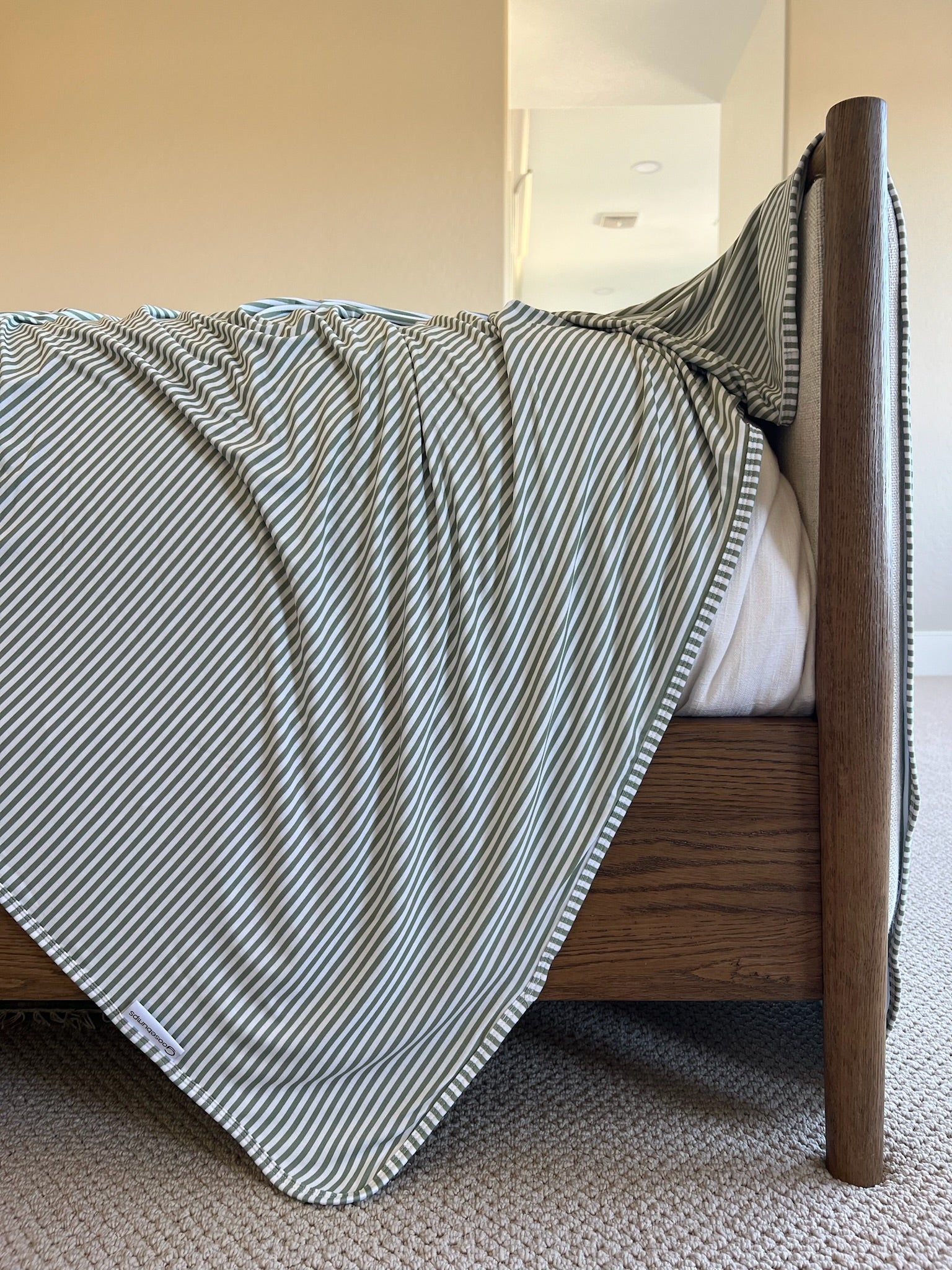 A close-up side view of the tree house bed with a luxurious green and white striped blanket draped over the edge in a carpeted bedroom featuring beige walls and natural light.