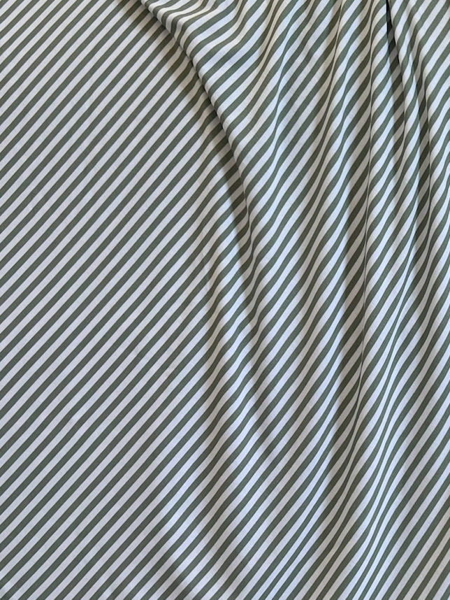 A close-up of the tree house / swaddle shows thin diagonal green and ivory stripes. The bamboo fabric is gently draped, creating soft folds and subtle shadows.