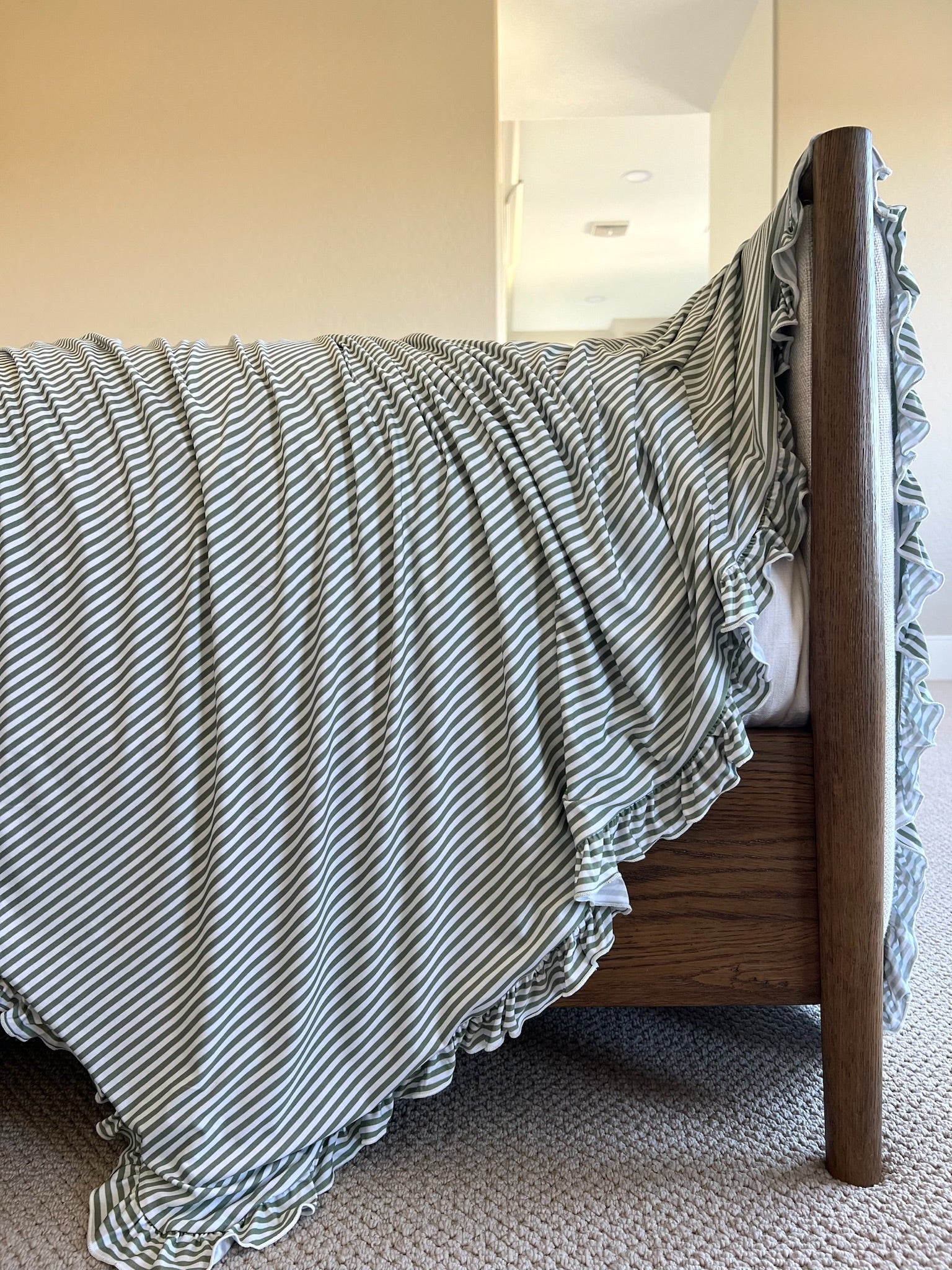 The tree house / ruffle bed frame features a vintage striped blanket draped over the side in soft folds, set against beige walls, a carpeted floor, and bathed in gentle natural light.