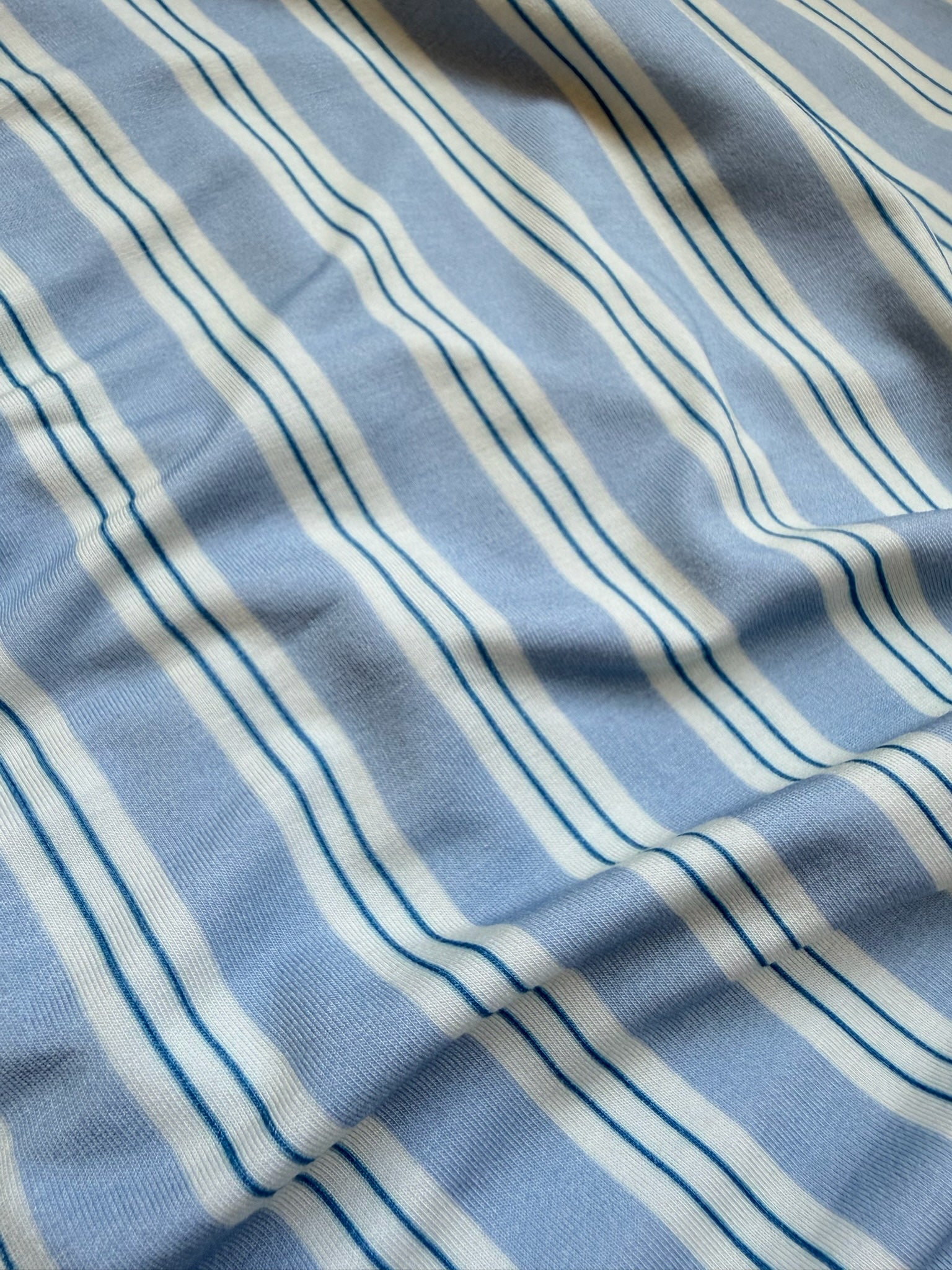 Light blue fabric with white and dark blue horizontal stripes, gently wrinkled to create soft shadows and texture across the surface—part of the Goosebumps Collection’s bamboo blanket series, haven adds a soothing touch to any space.