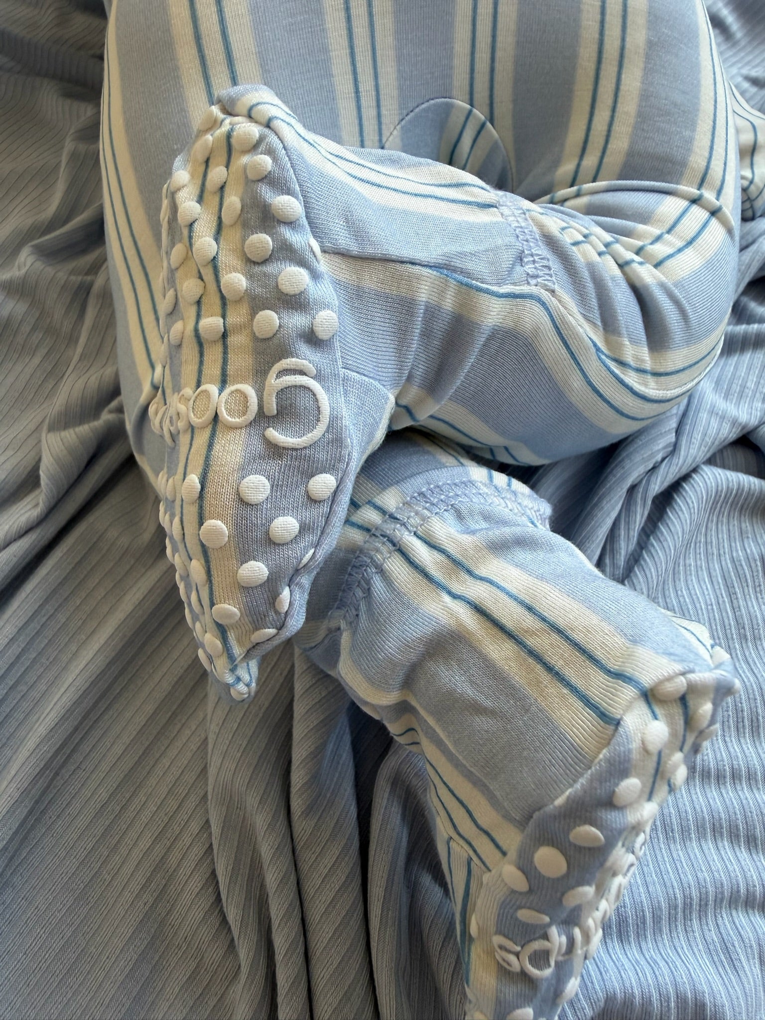 A cozy bamboo haven / one piece zipper sleeper with a convenient two-way zipper is displayed alongside a soft baby swaddle in blue and white stripes, featuring textured grips on the fabric’s edges, and a matching blue ribbed blanket—perfect essentials for your newborn.