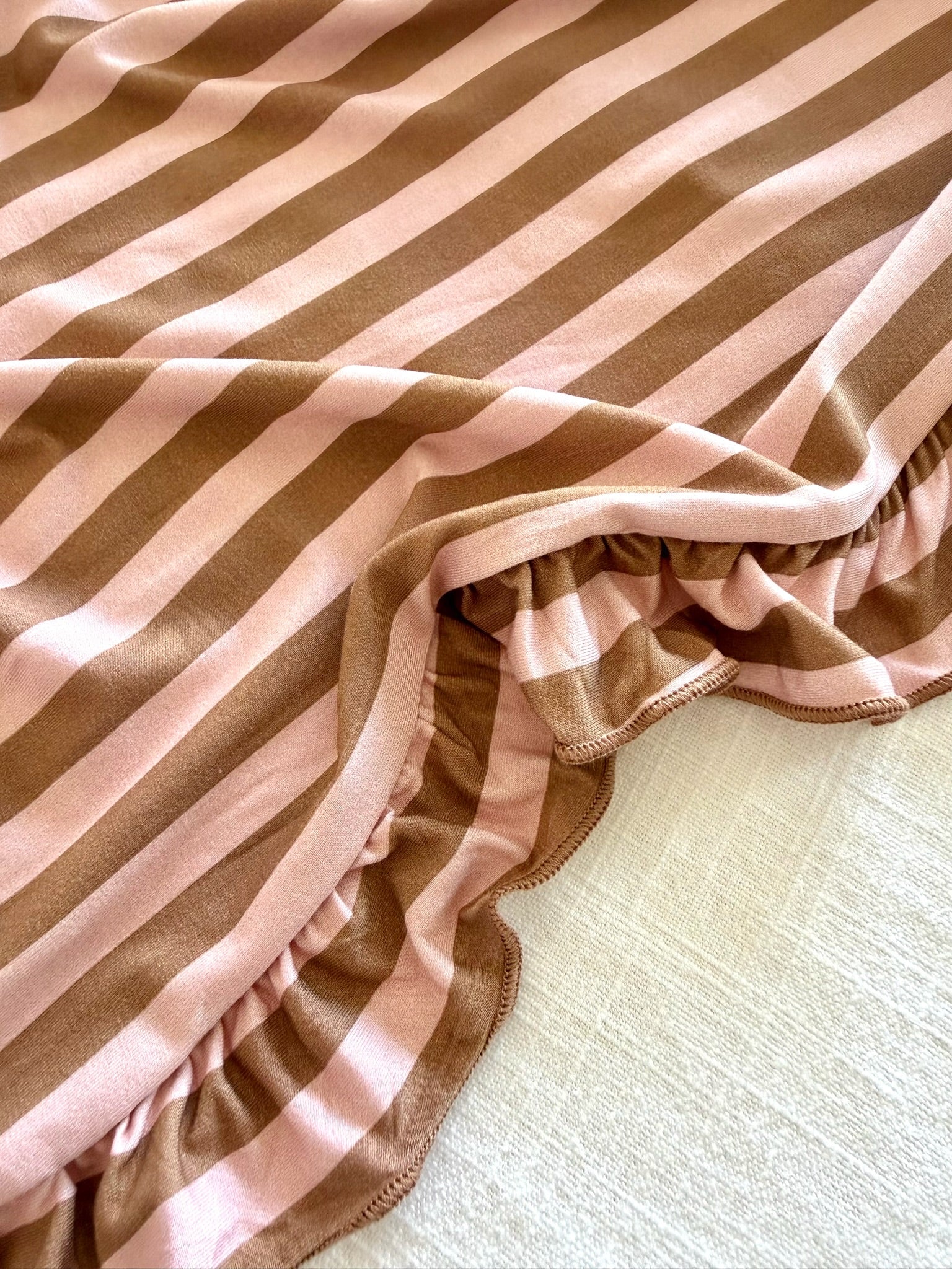 A close-up of the annabelle / ruffle blanket, crafted from soft bamboo and featuring wide, alternating light pink and brown stripes with elegant ruffled edges. The luxurious blanket is draped over a light, textured surface.