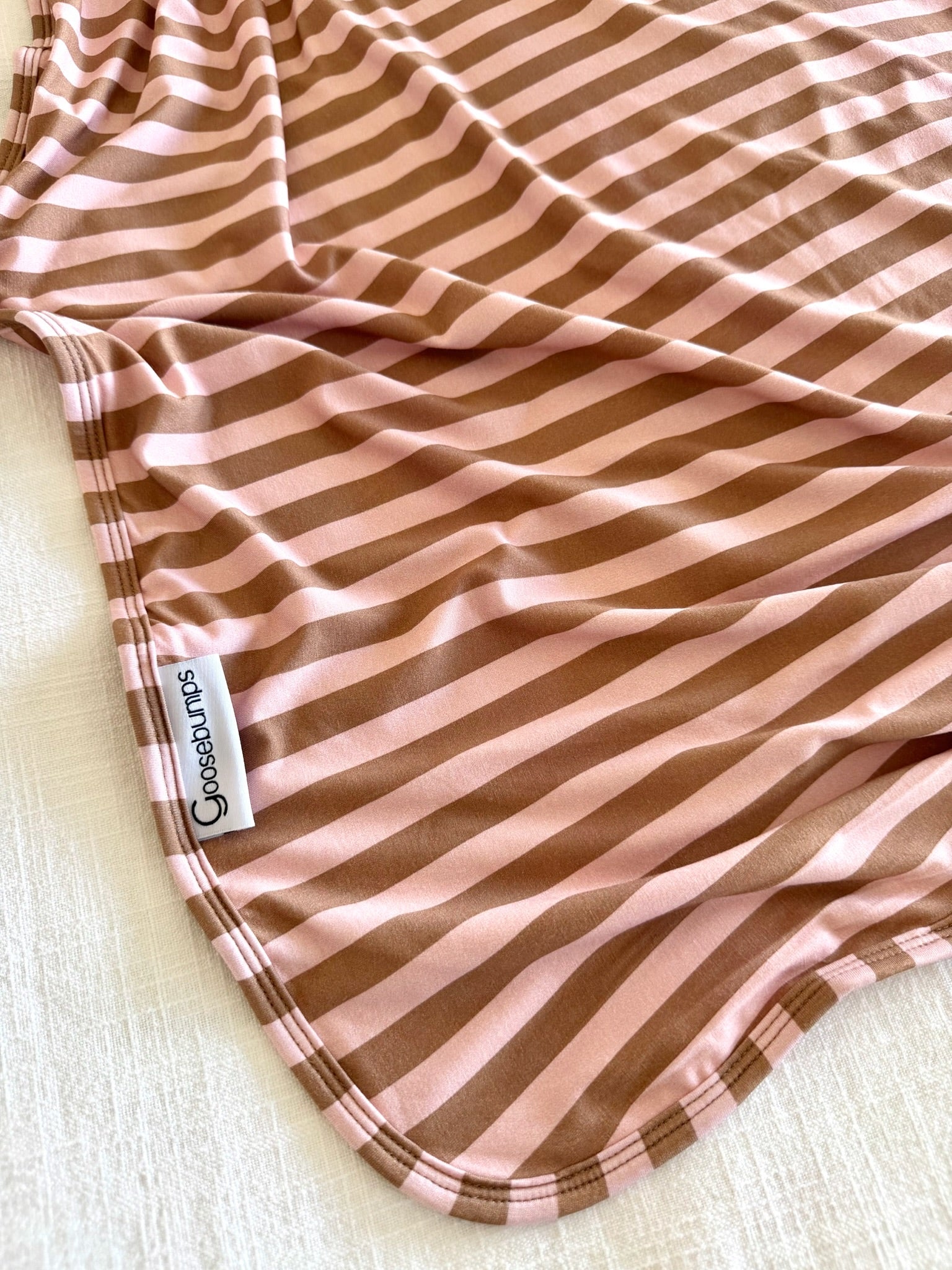 A pink and brown striped blanket named “annabelle” from Copper Pearl rests on a light, textured surface. Its neatly hemmed edges and gentle folds highlight the modern design and luxurious details of this stylish blanket.