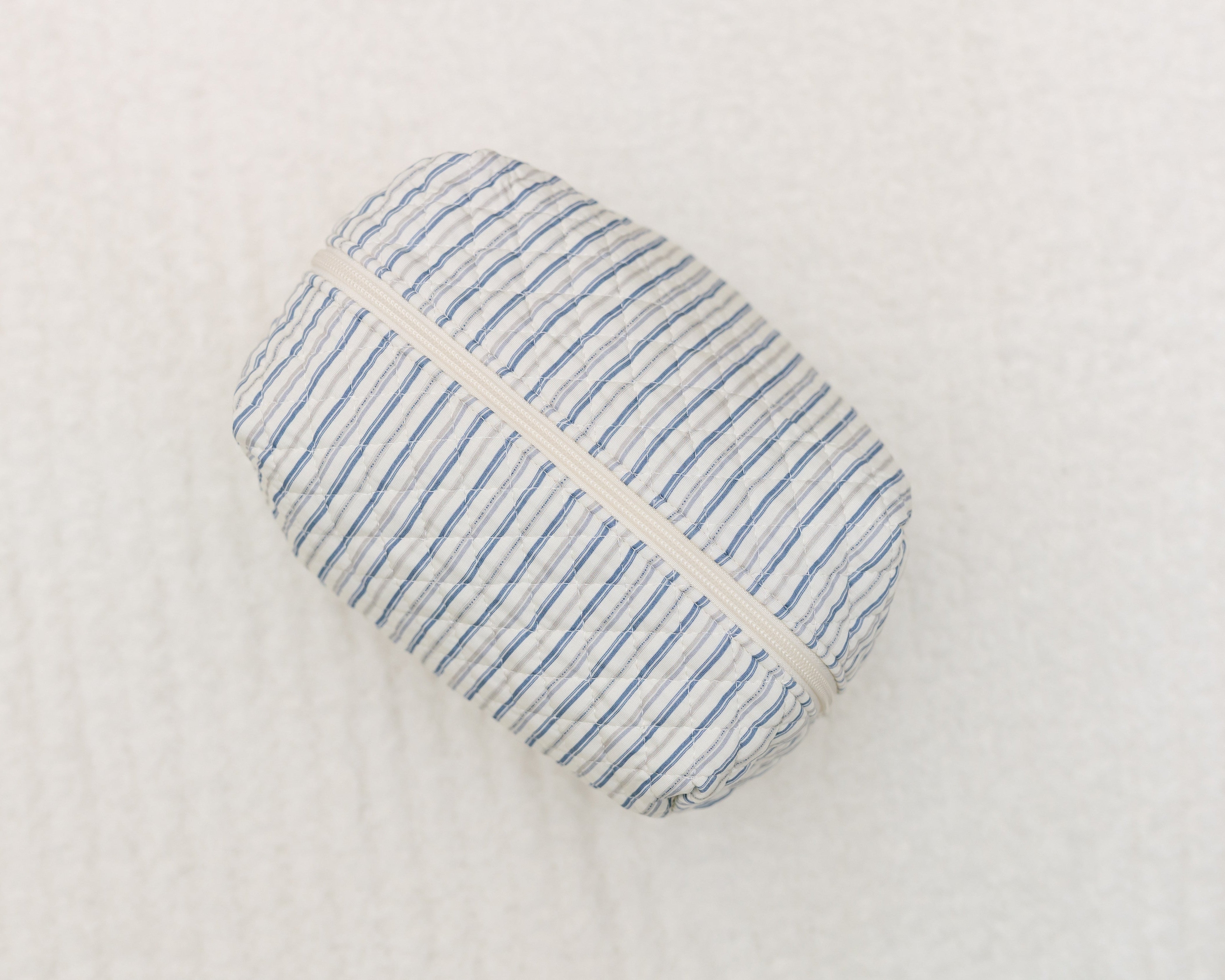 The beach house / travel bag is a small, rectangular travel accessory with blue and white vertical stripes and a white zipper—ideal for organizing your essentials on the go.