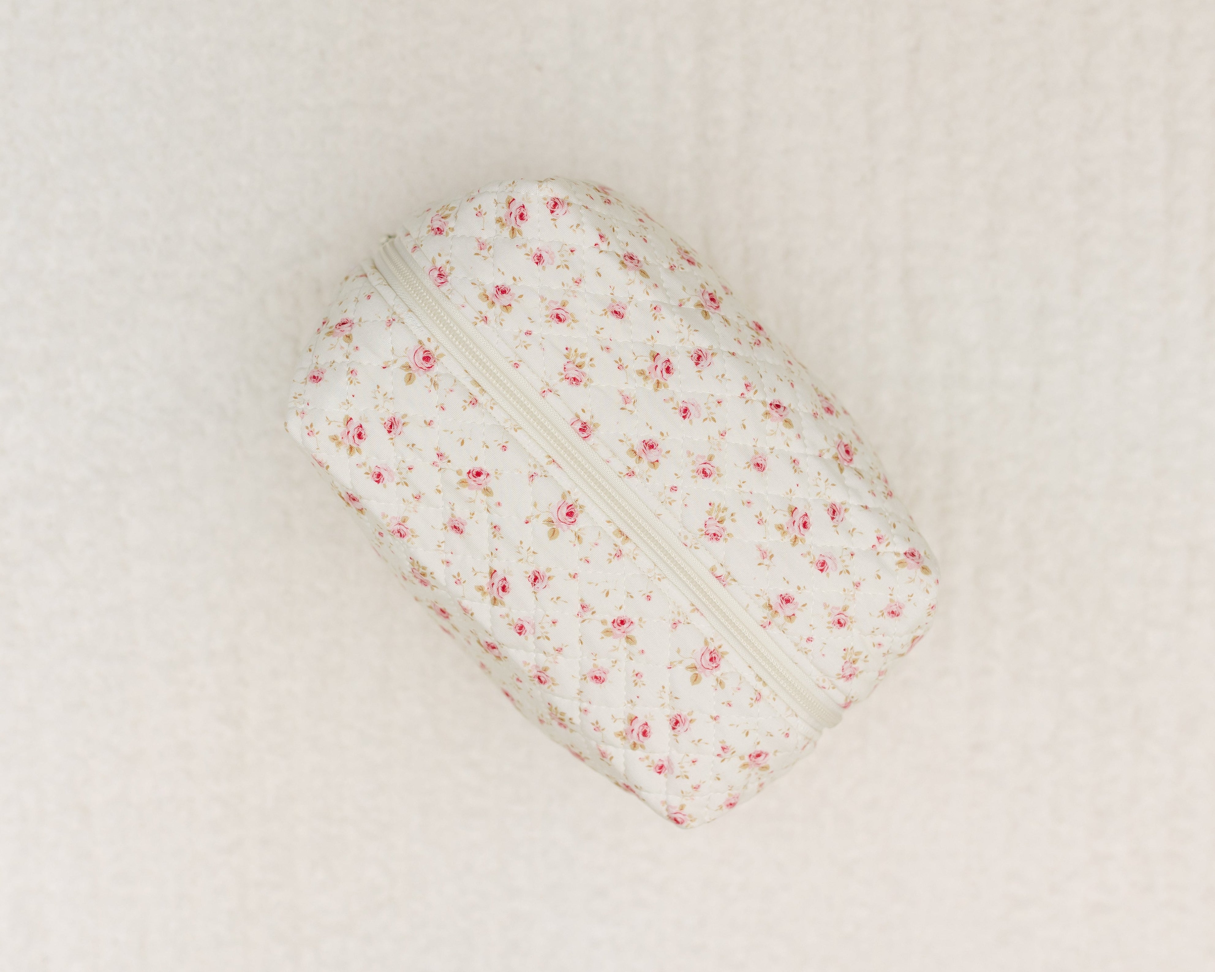 A small, rectangular afternoon tea / travel bag with a zipper, showcasing a white background and soft pink floral pattern, is displayed on a gentle, light surface.