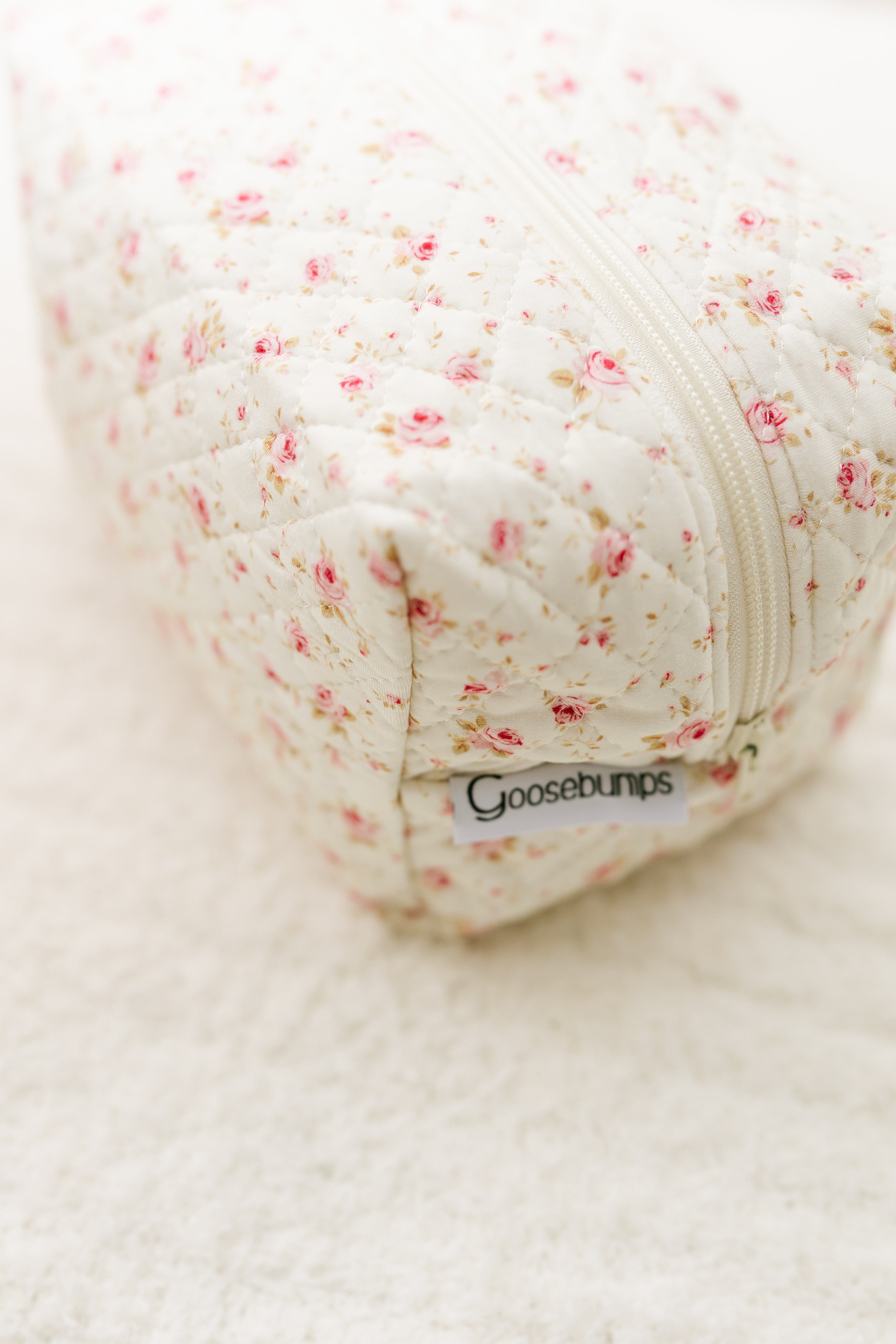 A close-up of the afternoon tea / travel bag with a floral print, quilted fabric, zipper, and signature label—perfect for travel and shown resting on a soft, textured surface.