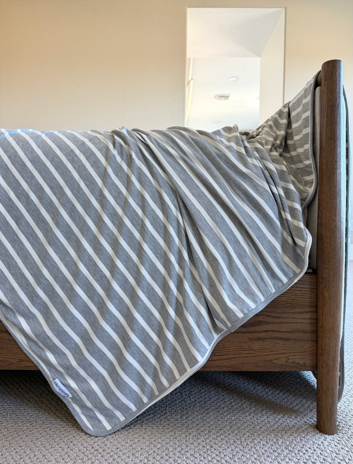 A luxurious heather grey and white striped timeless blanket draped over the foot of a wooden bed.