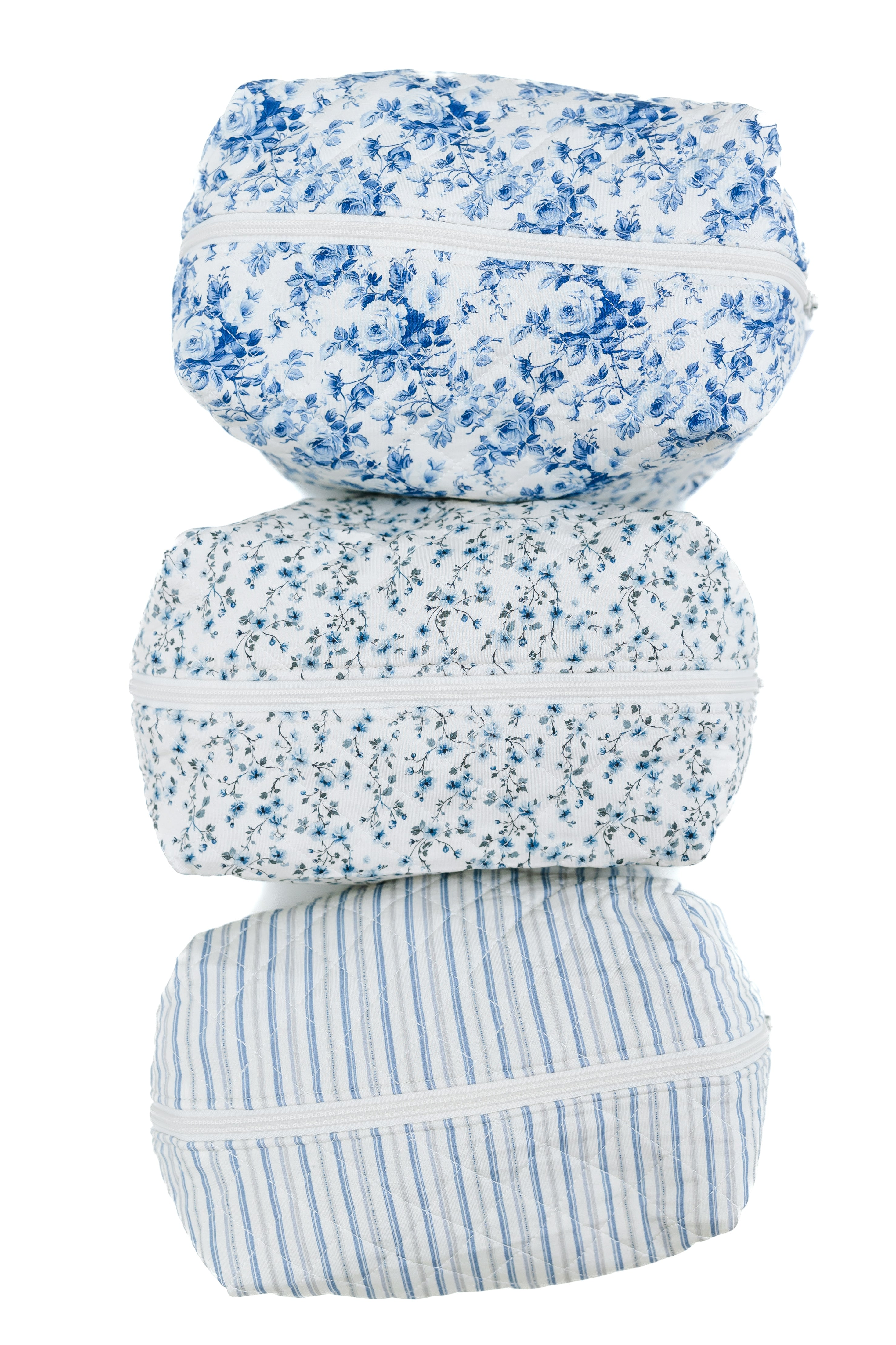 The cottage / travel bag set includes three zippered pouches stacked vertically, each with a unique blue and white design: a floral print on top, tiny flowers in the middle, and vertical stripes on the bottom.