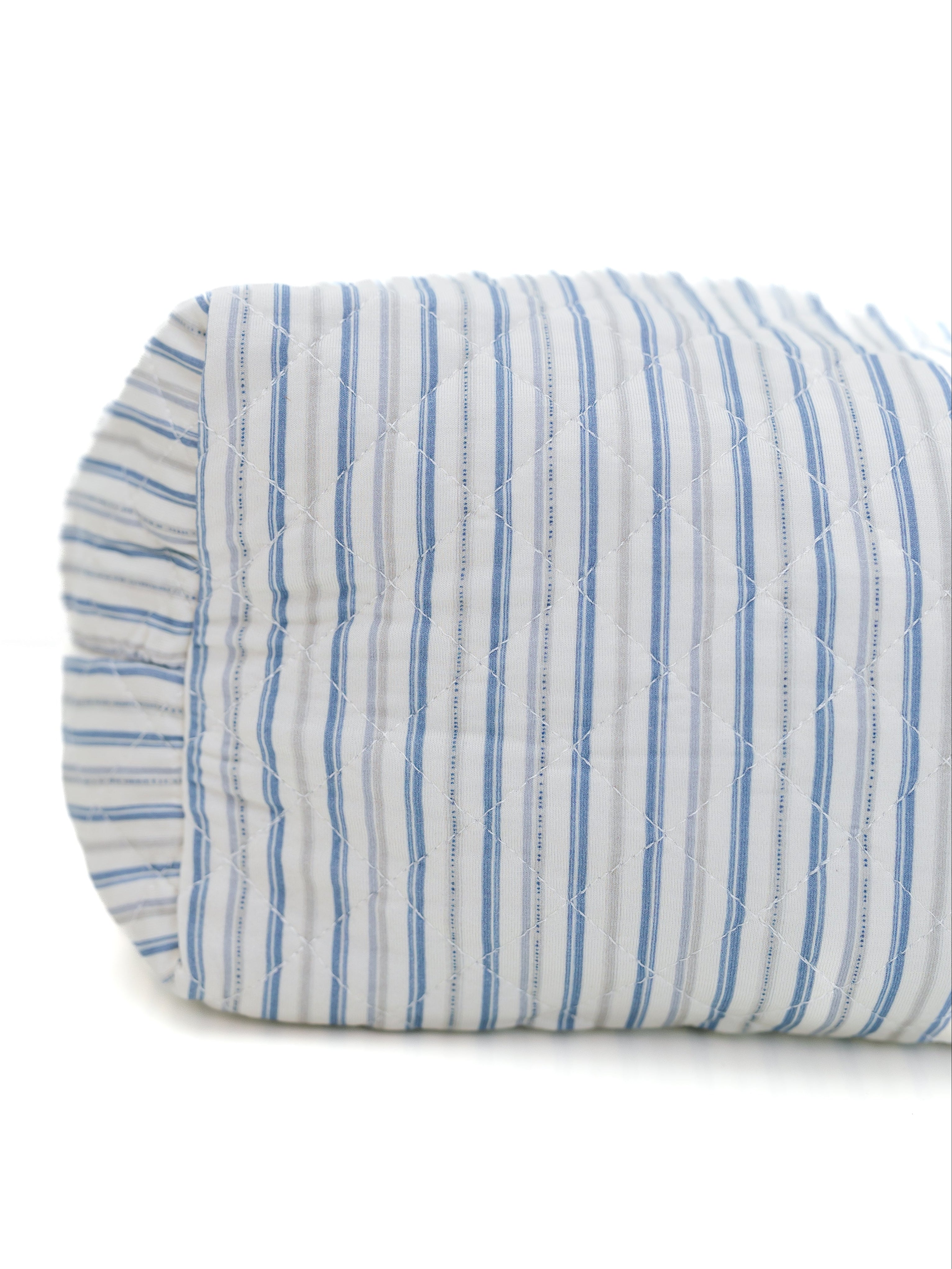 The beach house / travel bag, shown rolled up with a white background and blue vertical stripes, is the perfect travel accessory—ideal for cozying up or using as an adult swaddle bag wherever you go.