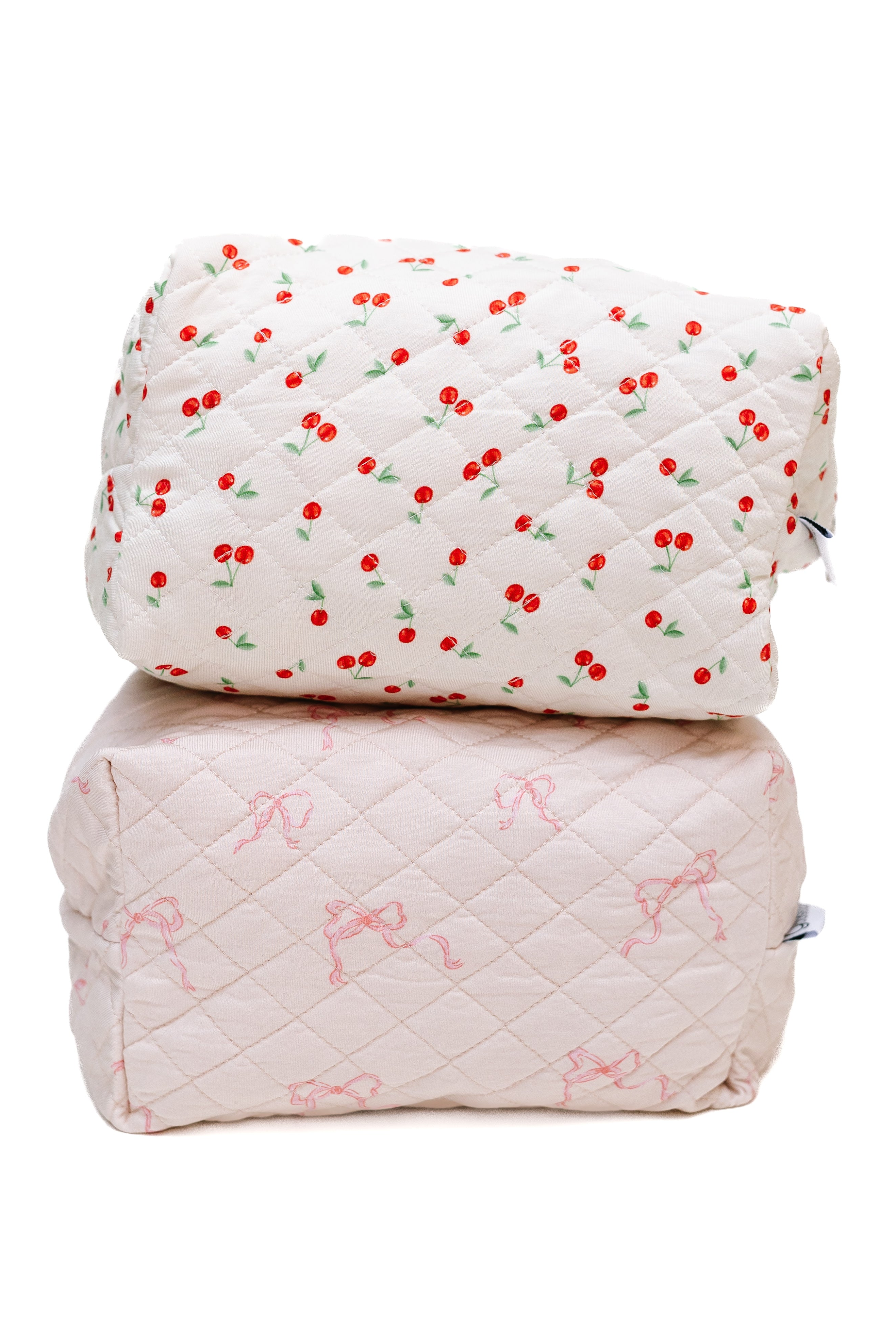 The "cherry on top / travel bag" set includes two quilted pouches: one with a red cherry pattern and another in pale pink with a ribbon bow, making them an adorable accessory for any trip.