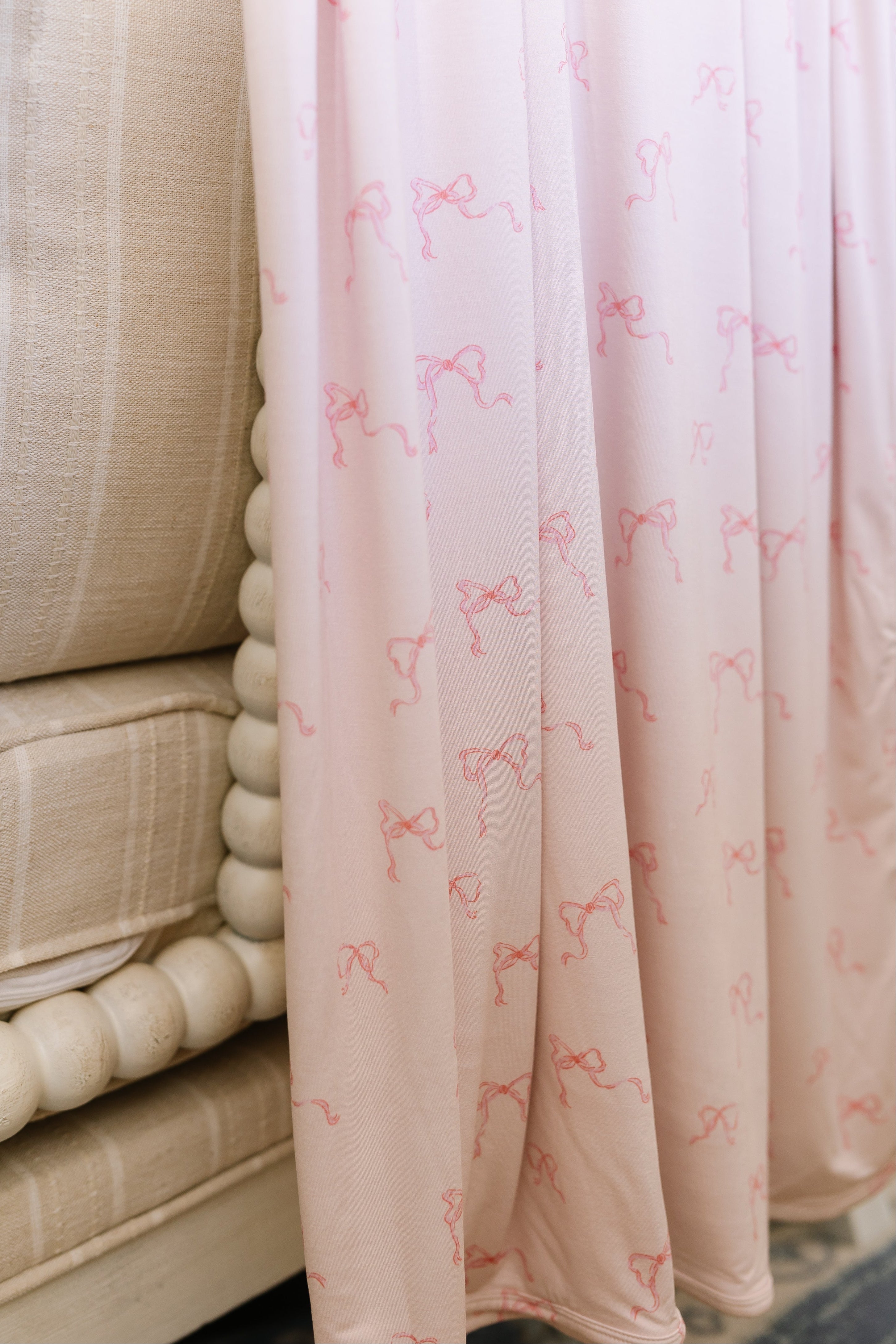 The "ballerina" blanket, in soft light pink with a small bow pattern, drapes over a cream spindle-leg chair topped with a beige striped cushion.