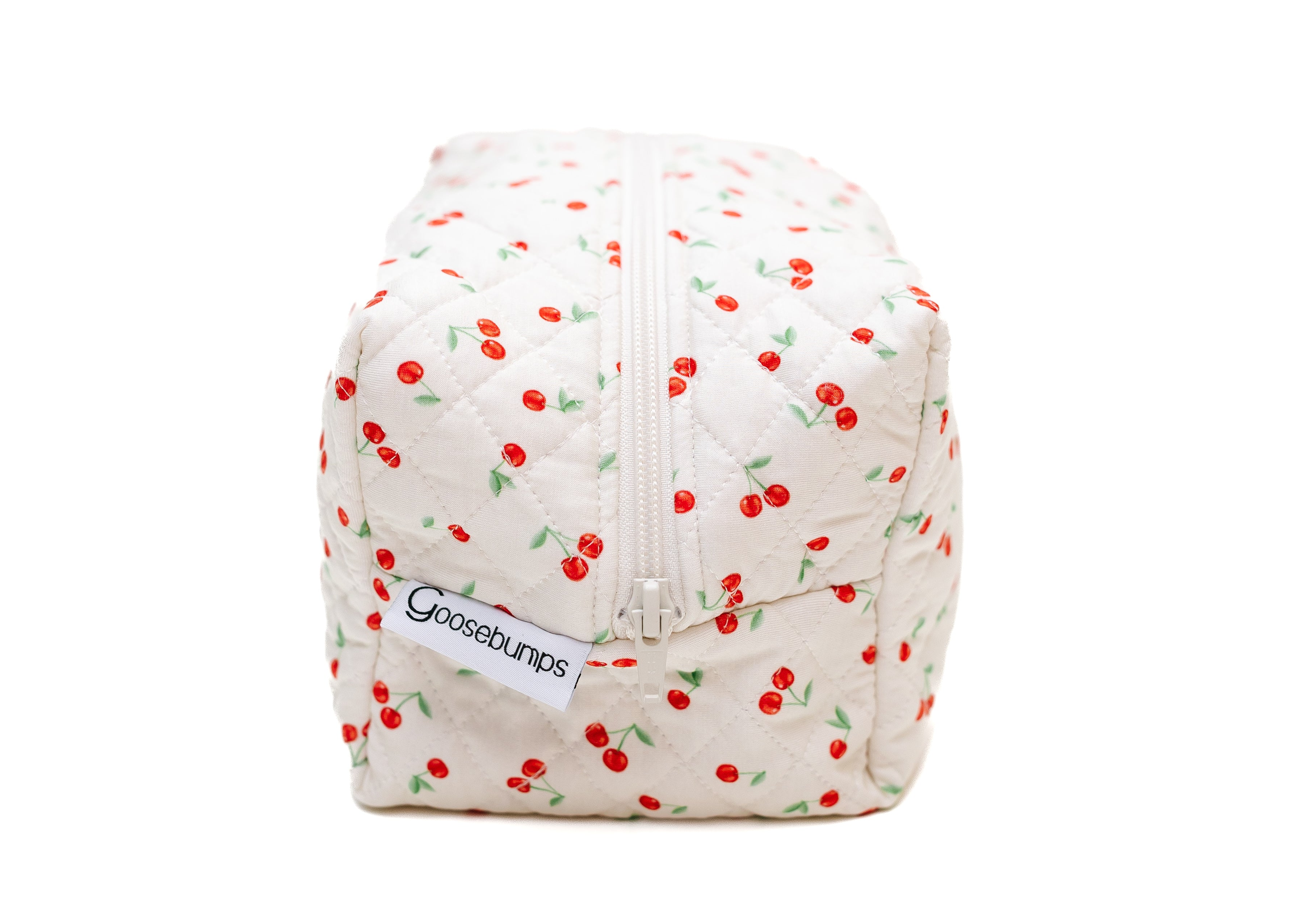 The cherry on top / travel bag is a white quilted pouch with a cherry pattern and top zipper, ideal for cute travel essentials. A side tag features the cherry on top branding.