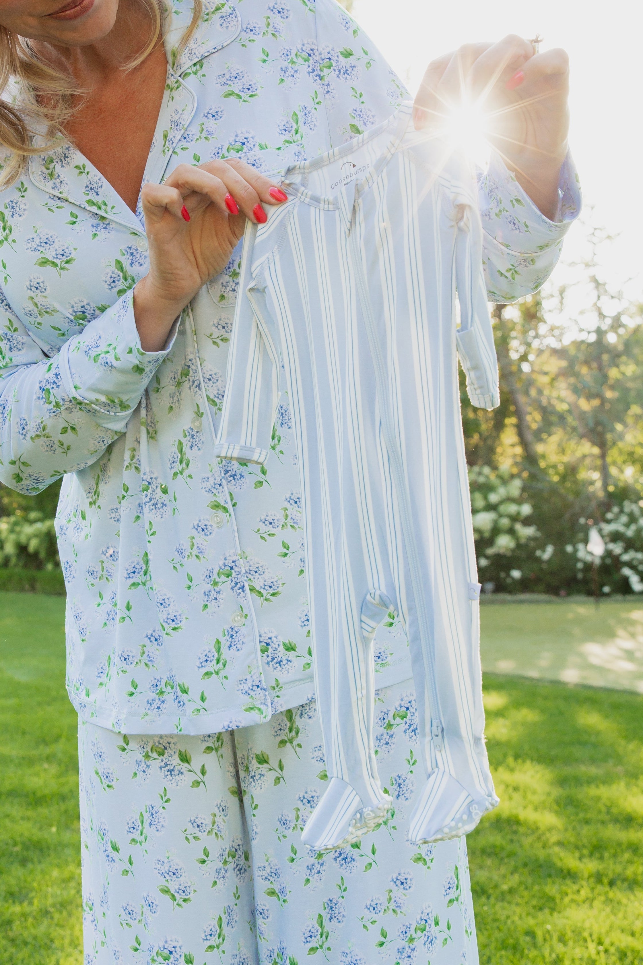 A person in floral pajamas holds up a haven / one piece zipper in blue and white stripes outside, with sunlight shining through its buttery-soft fabric.