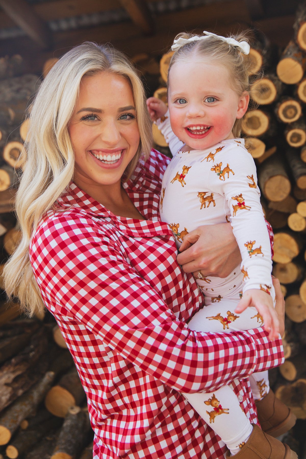 A woman in a red and white gingham checkin’ it twice / pajama set / long pant holds a toddler wearing pajamas printed with reindeer.