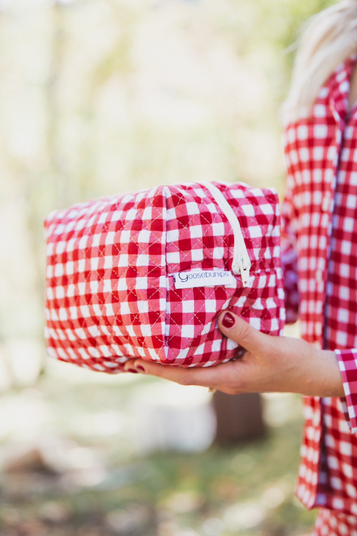 Person holding a quilted red and white gingham checkin’ it twice / travel bag with a zippered closure.