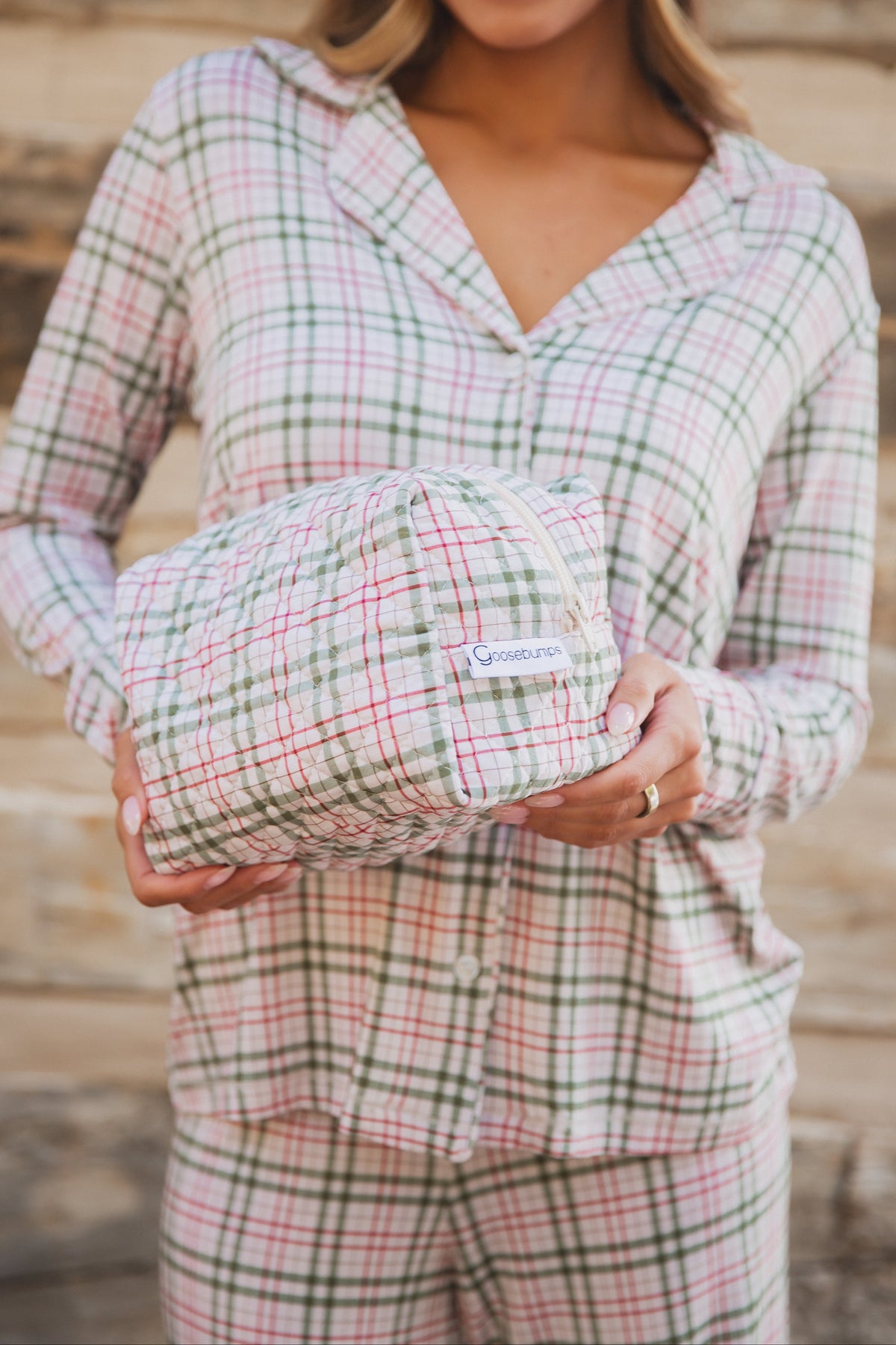 A person in matching plaid pajamas holds a rectangular quilted homestead / travel bag featuring a green and red grid pattern.