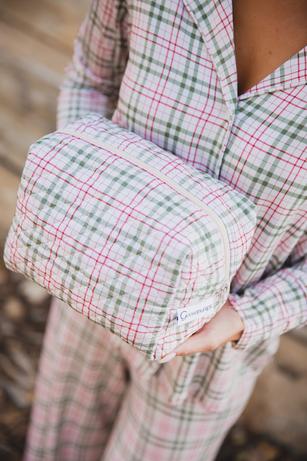 A person wearing matching red, green, and tan plaid pajamas holds a homestead / travel bag in the same pattern.
