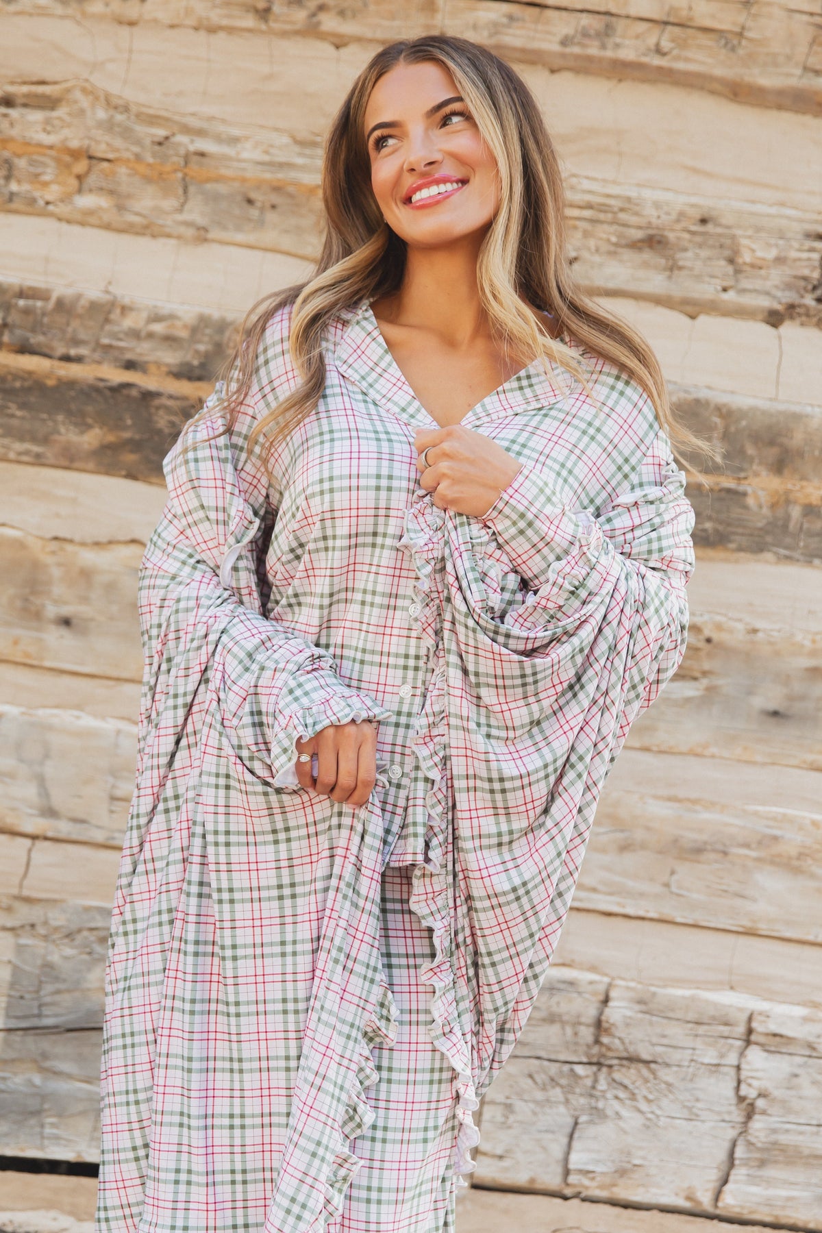 A woman wearing the homestead / ruffle, a long-sleeved, button-up plaid shirt with ruffled trim that matches the aesthetic of a luxurious plaid blanket.