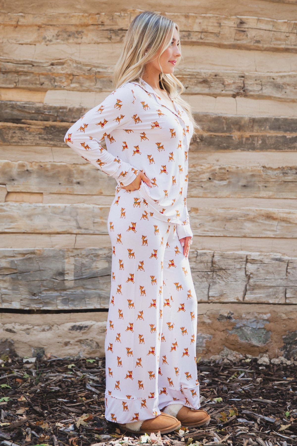 A woman standing in profile wearing a vintage reindeer pajama set with a long-sleeved button-up top and matching wide-leg long pants.
