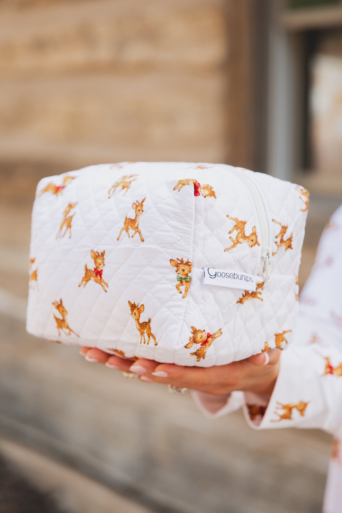 Hands holding a white quilted vintage reindeer / travel bag featuring a repeating print of cartoon reindeer.