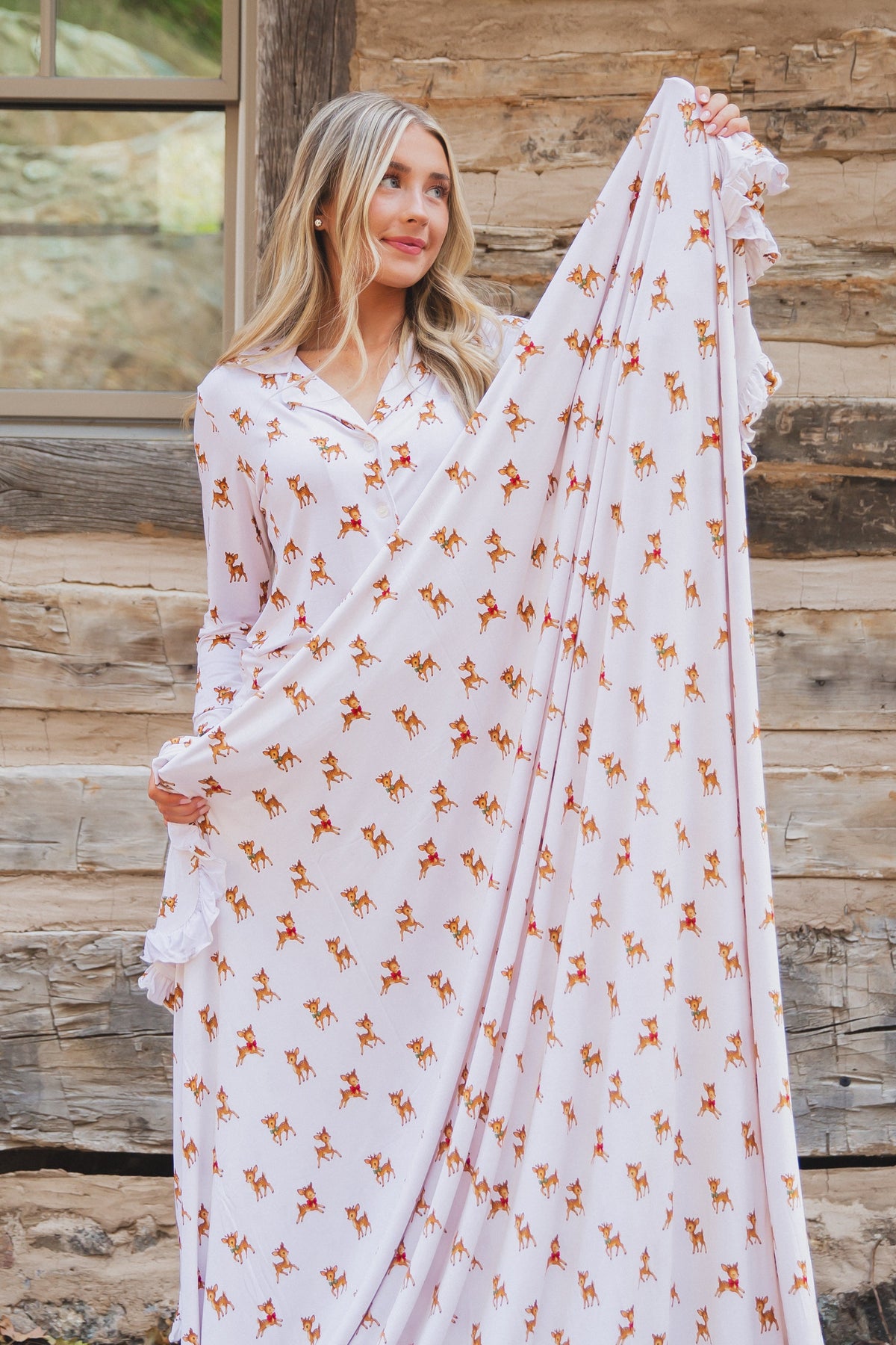 A woman wearing a long-sleeved vintage reindeer / ruffle nightgown with ruffled edges, holding the fabric up to display the print.