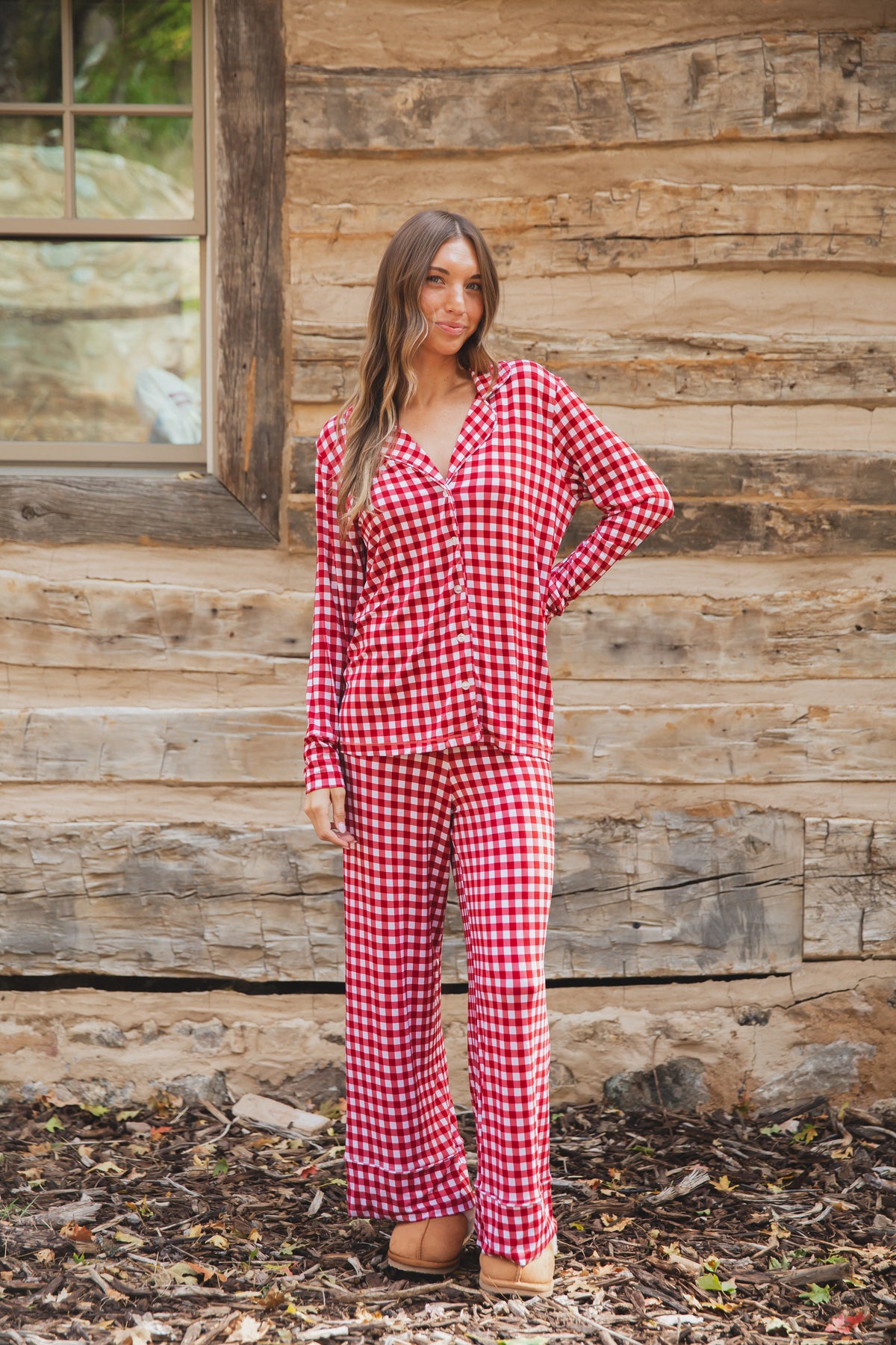 A woman wearing a red and white gingham checkin’ it twice pajama set with a button-down top and matching long pants.
