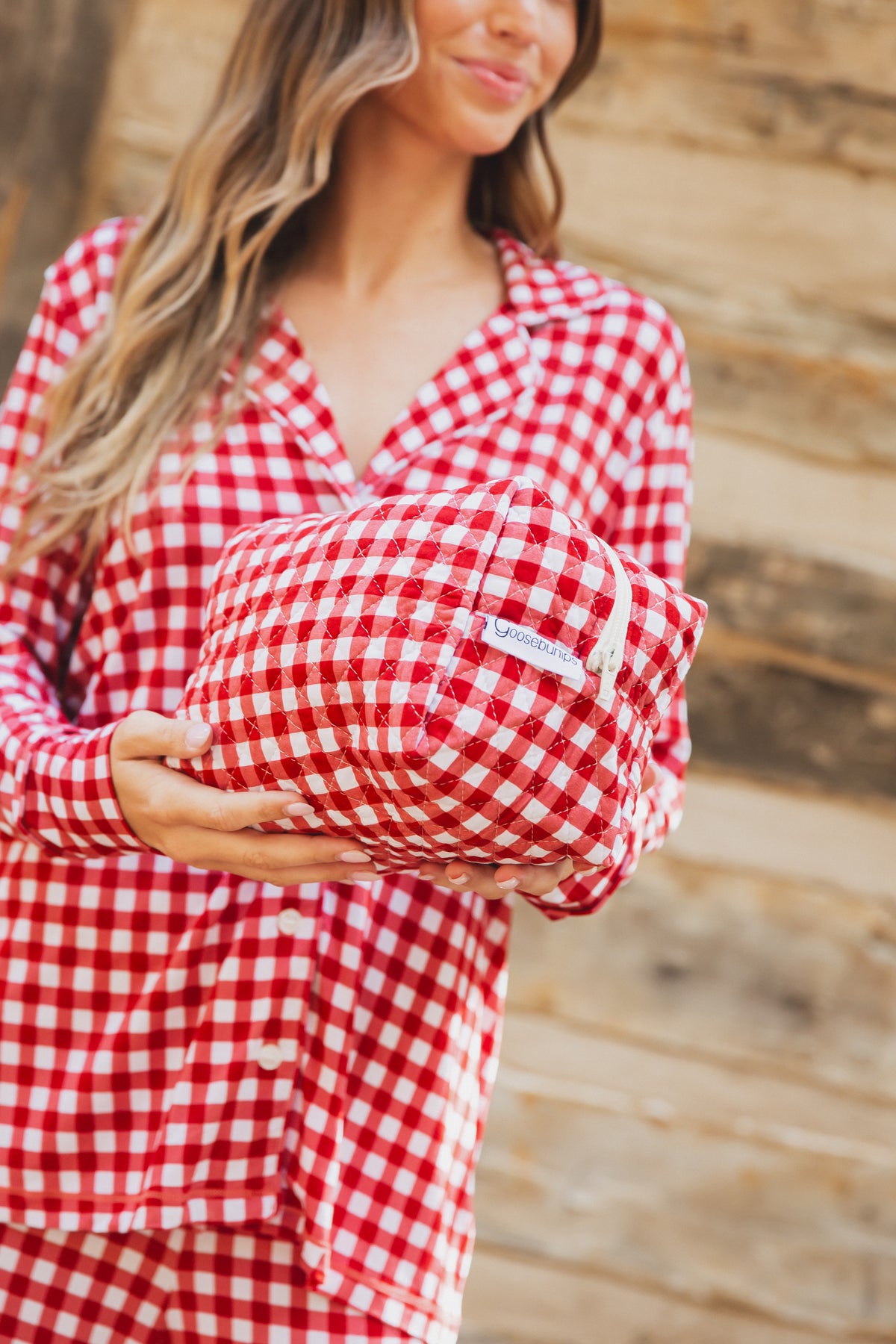 A person wearing red and white gingham pajamas made from viscose from bamboo holds a matching checkin’ it twice / travel bag.