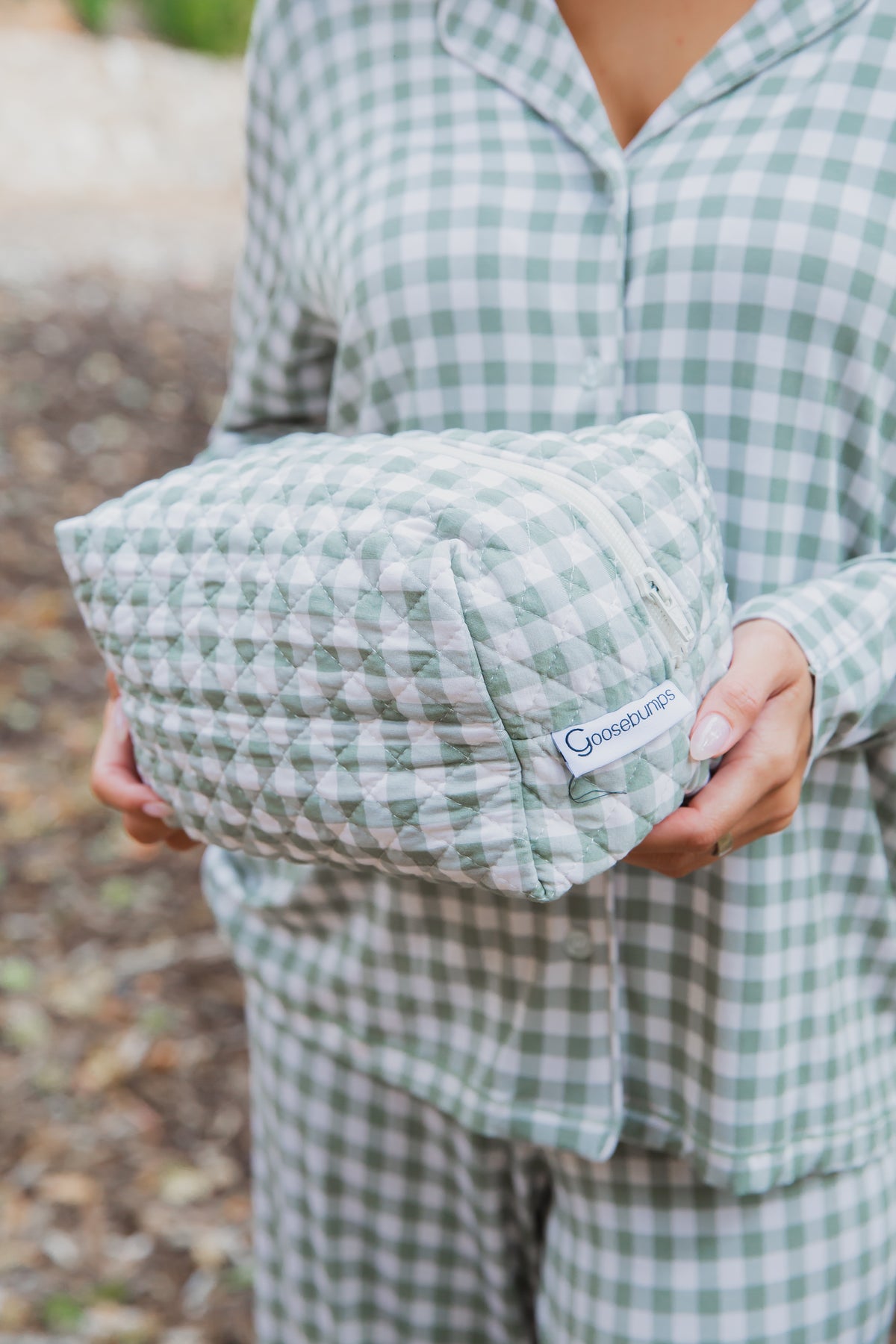 A person holding a green and white gingham quilted evergreen lane / travel bag with a zippered closure.