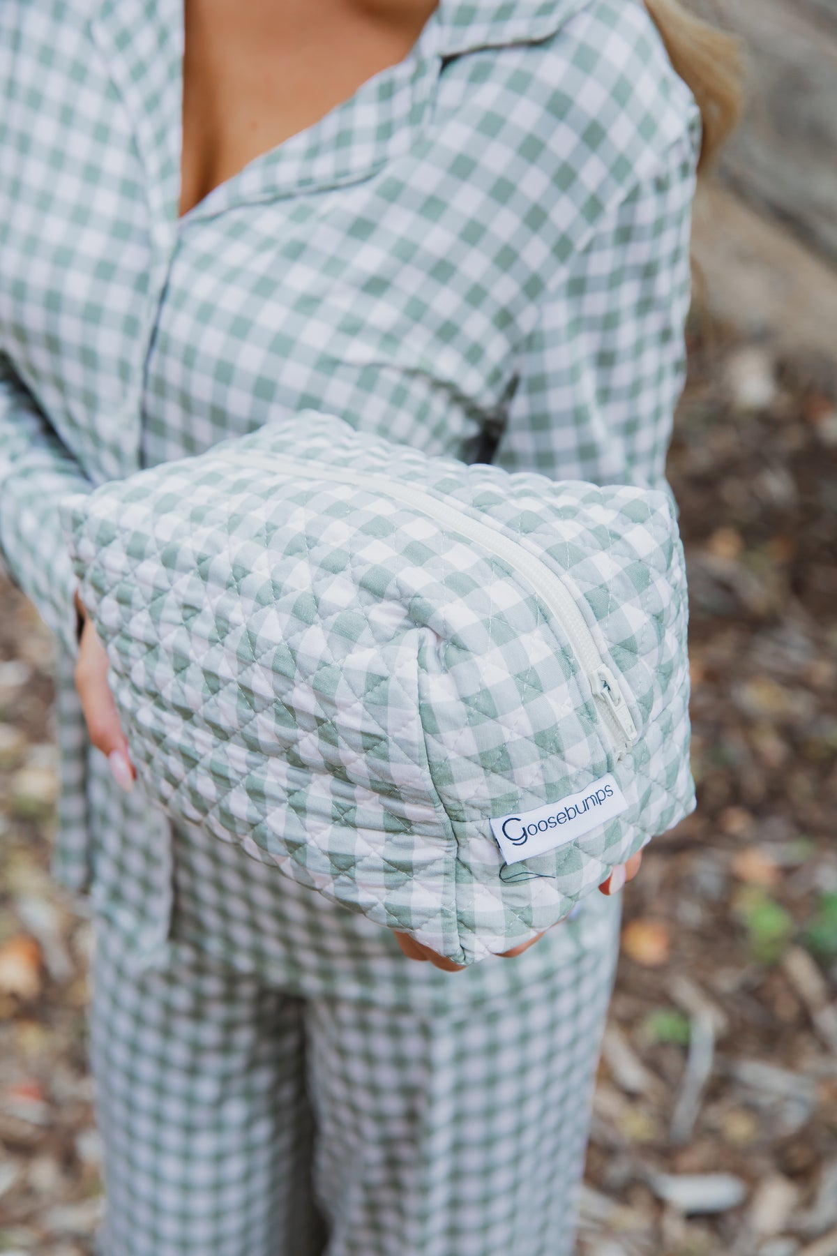A person in a green and ivory gingham viscose from bamboo pajama set holds a matching evergreen lane / travel bag featuring a quilted design and zippered closure.