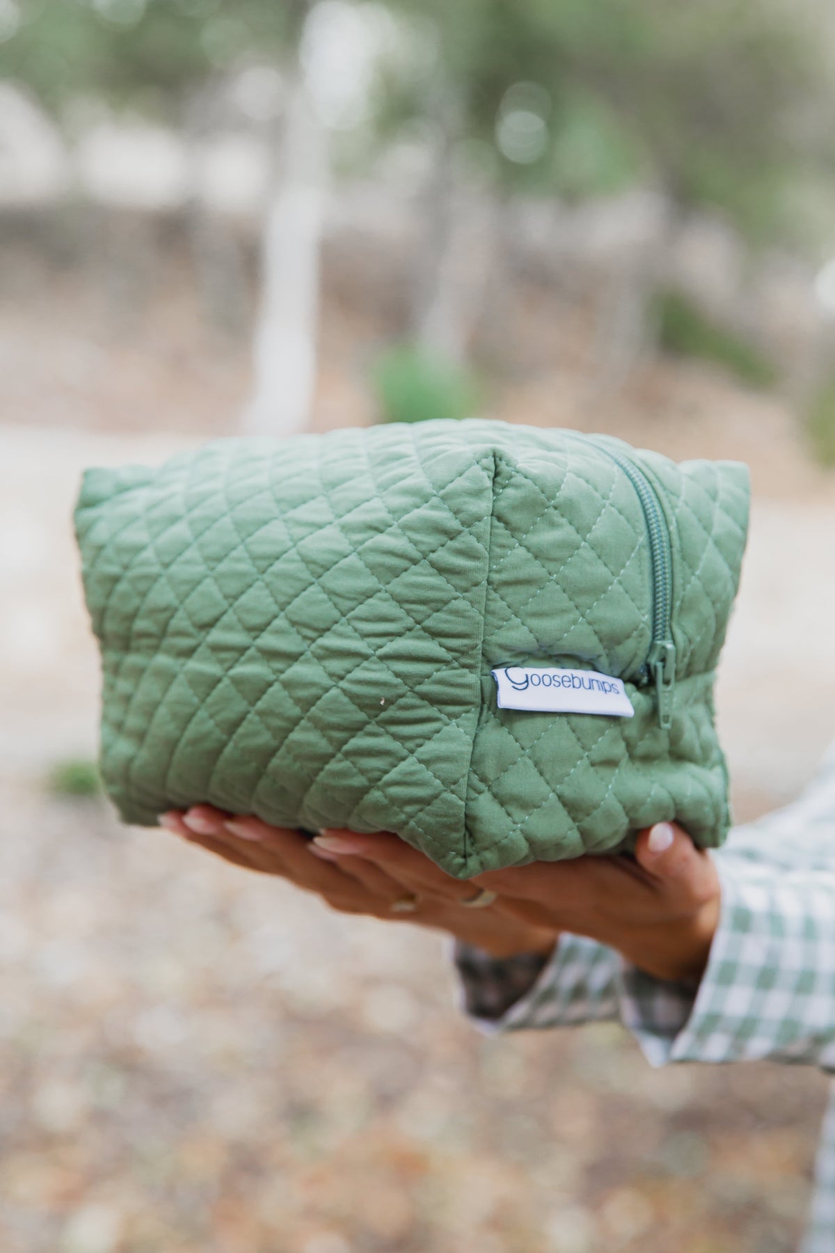 Hands holding a winter pine travel bag, a quilted sage green design made from bamboo viscose and spandex with a zippered closure.
