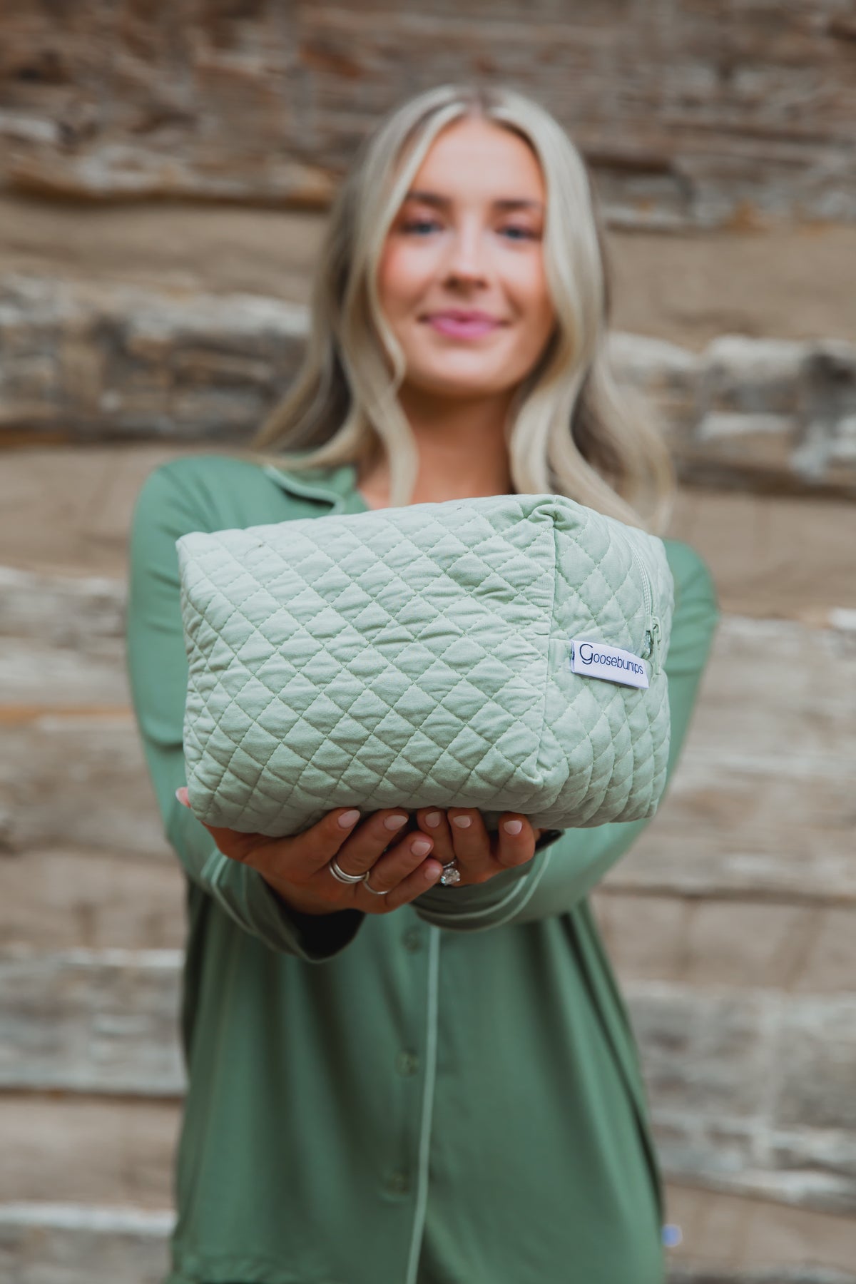 A person holds a solid sage green, quilted bamboo viscose frosted fir travel bag with a zippered closure.