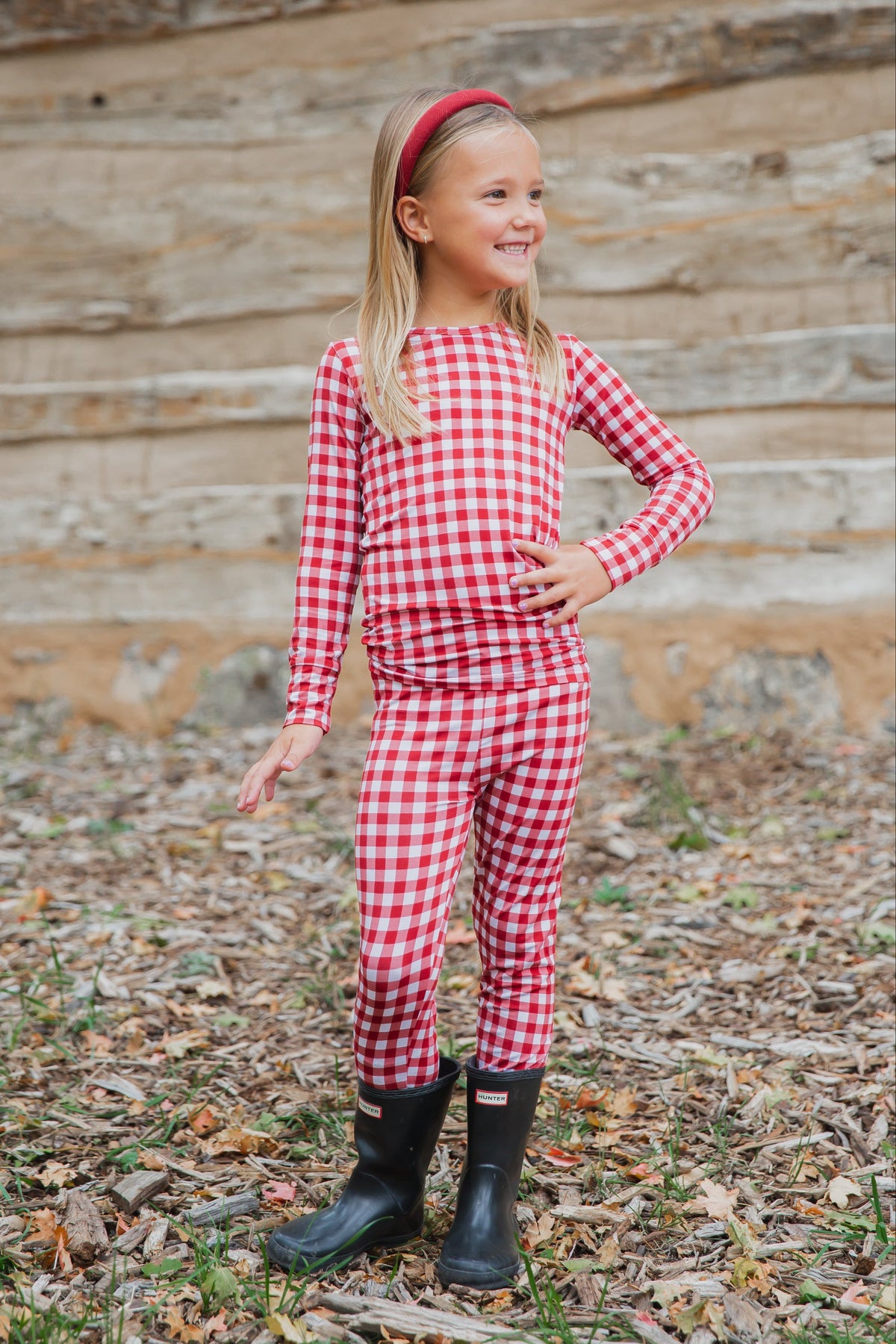 A young girl wears checkin’ it twice / two piece skinny—cozy red and white gingham sleepwear—paired with black rain boots.