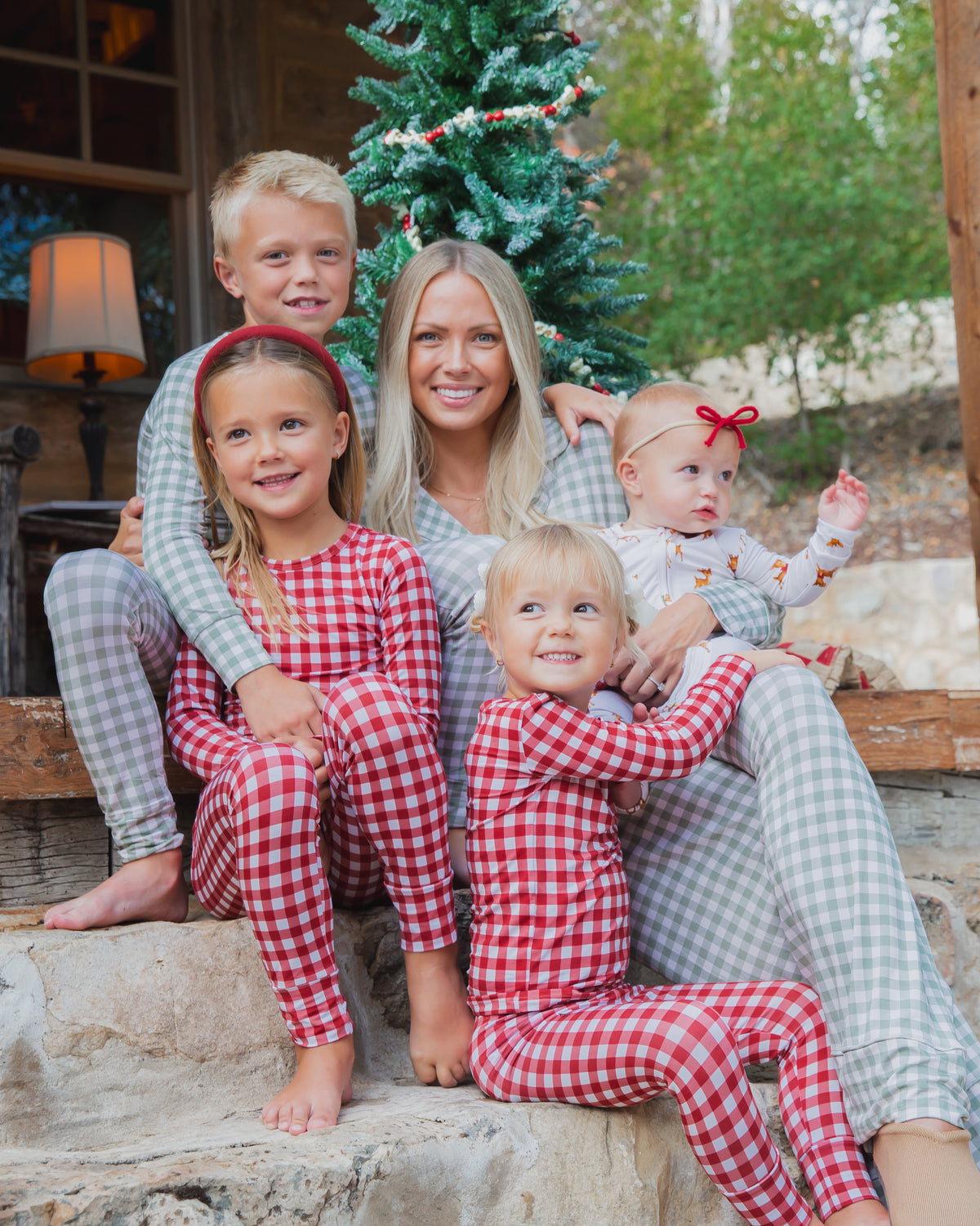 A woman sits on stone steps with her four children, all wearing matching green and ivory gingham evergreen lane / two piece skinny bamboo pajamas.